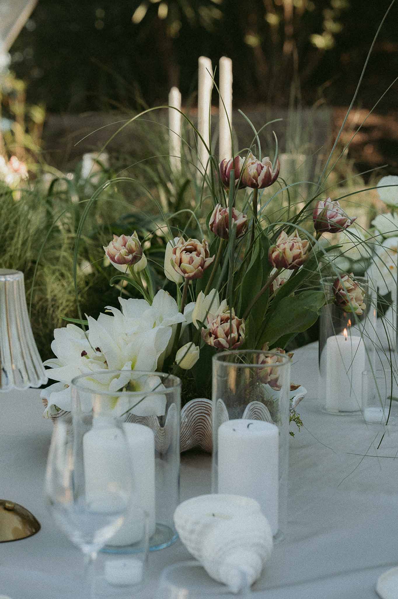 Reception centerpiece of dusty mauve tulips white amaryllis and taper candles in glass cylinders