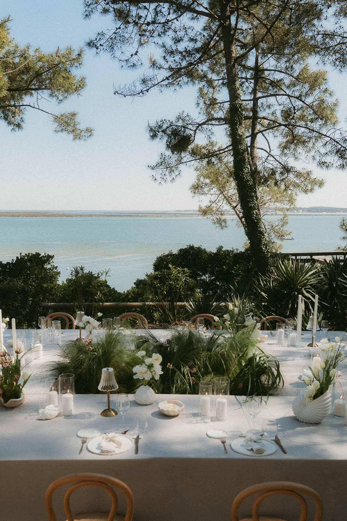 Outdoor reception table on terrace overlooking bay with white peonies, pampas grass, and gold cutlery