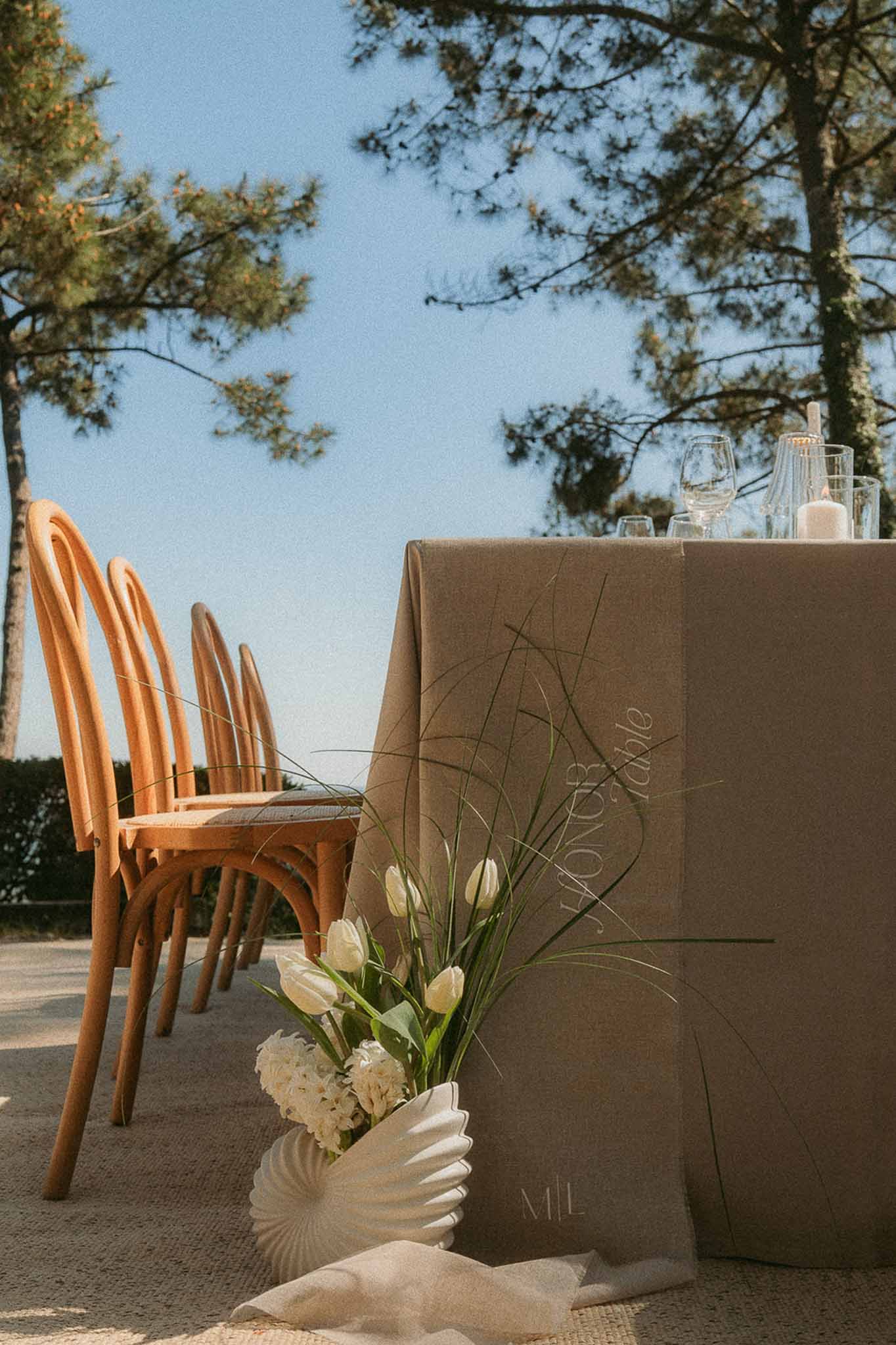 Head table with calligraphy linen, bentwood chairs, and white tulip arrangement in ribbed ceramic vase