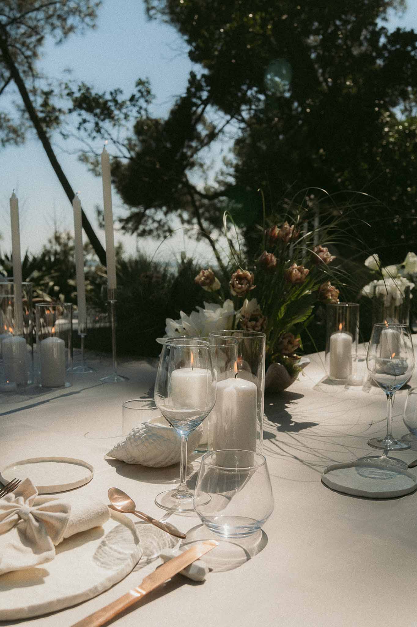 Outdoor reception table with rose gold flatware shell decorations dusty mauve tulips and taper candles at dusk