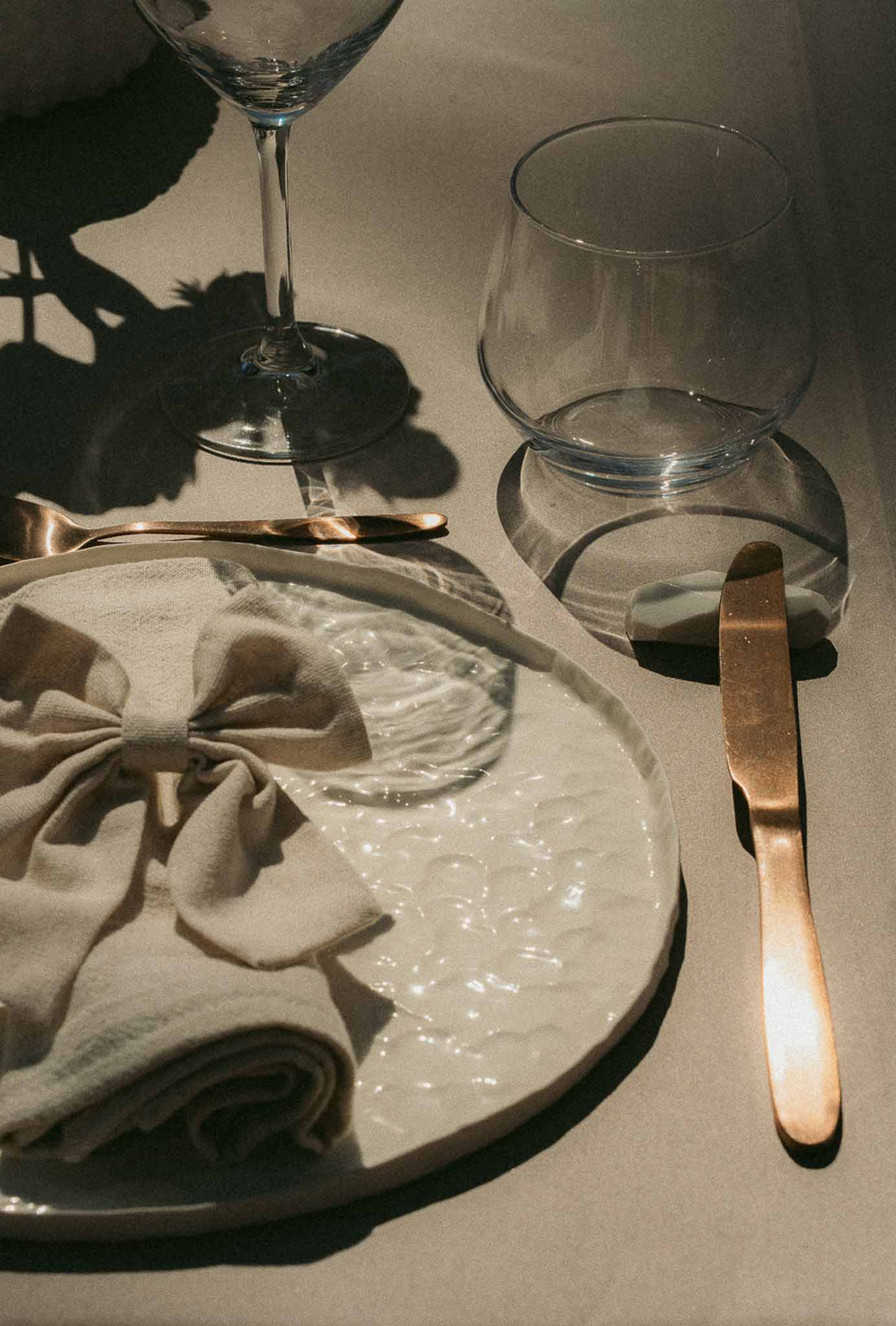 Place setting with ivory plate, linen bow napkin, brushed gold flatware, and stemmed glasses on taupe linen
