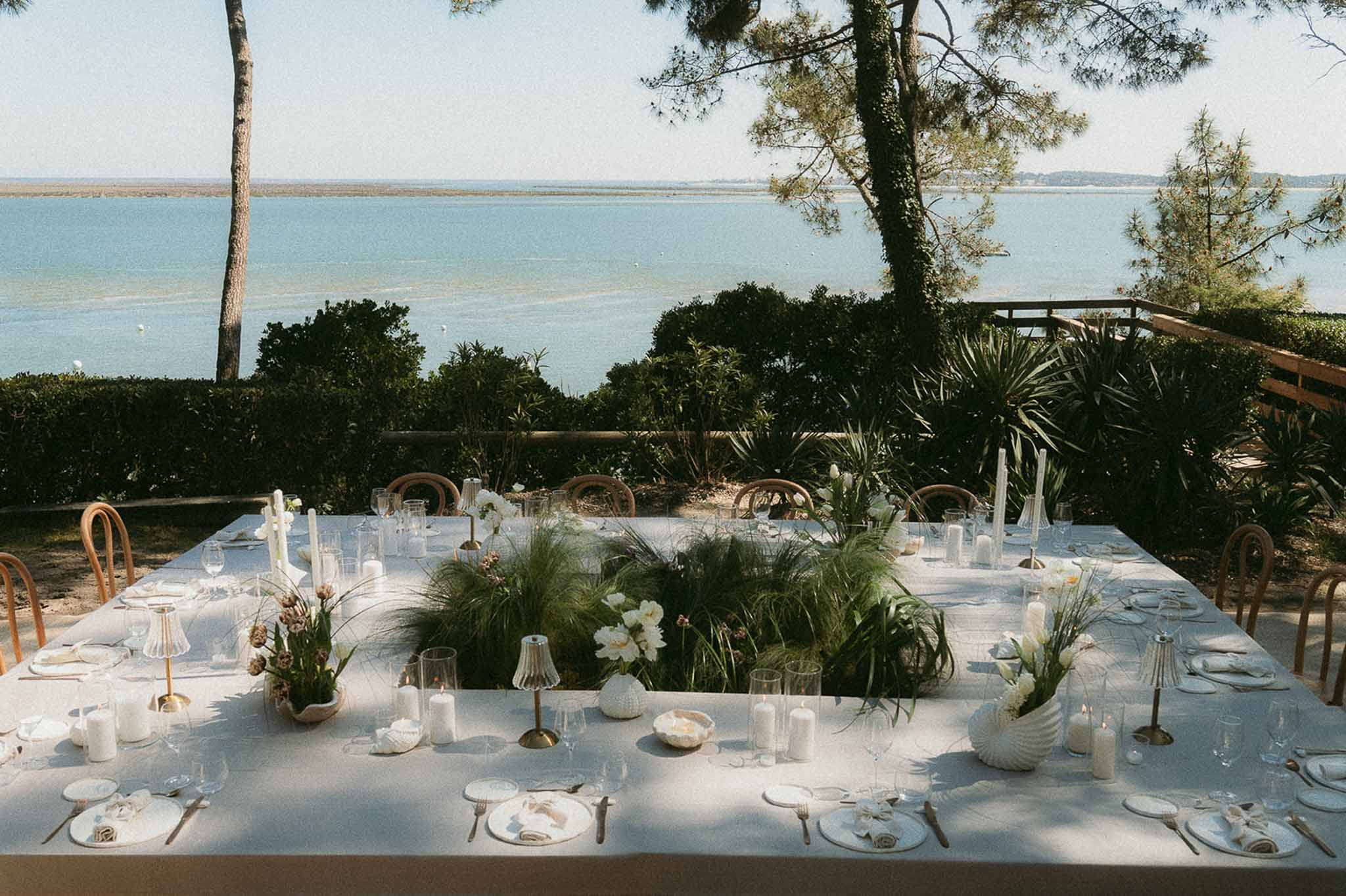 Coastal table with peonies, sea urchin shells, brass candlesticks, and bentwood chairs overlooking bay