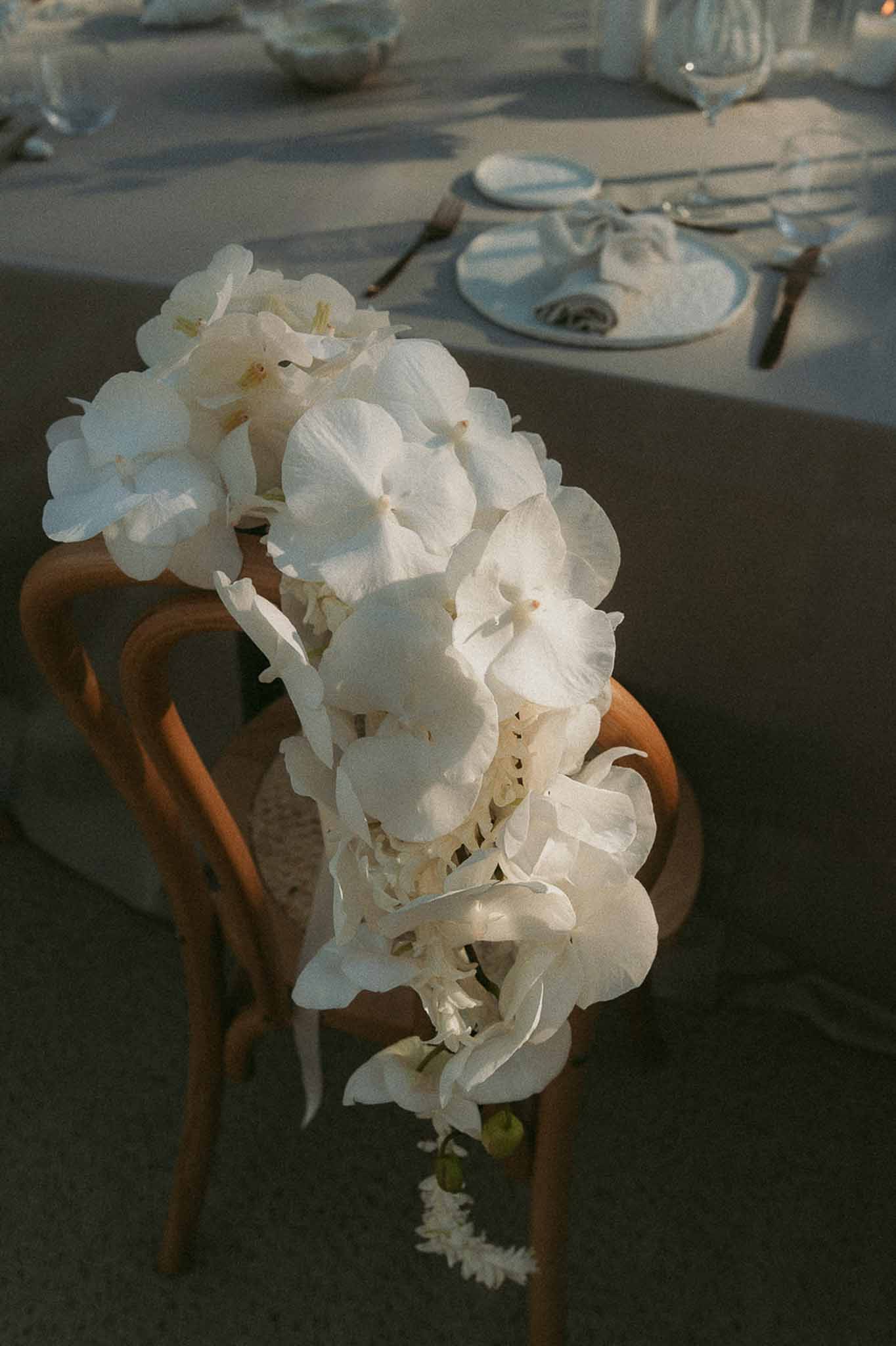 Cascading white hydrangea and phalaenopsis orchid arrangement draped over crossback reception chair