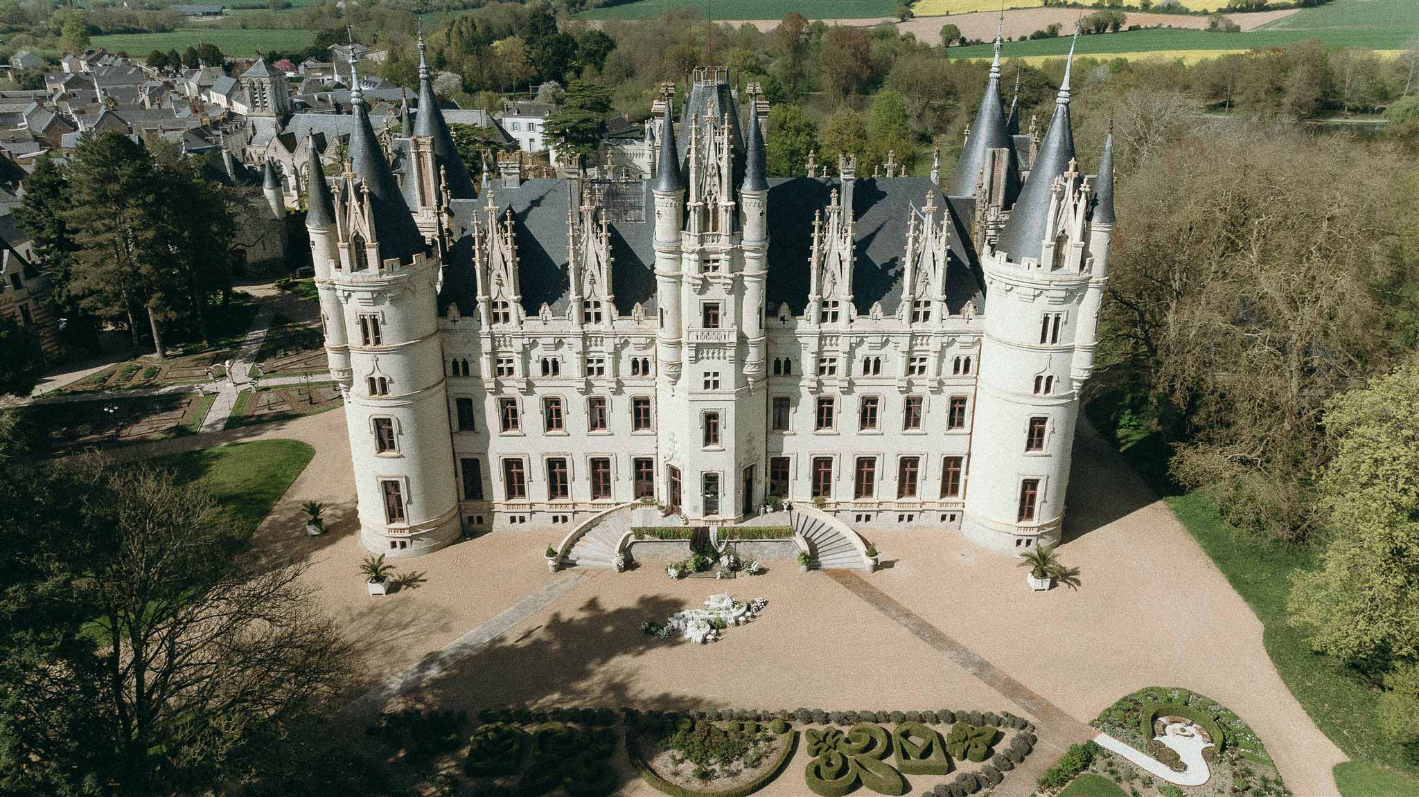 Aerial view of Gothic chateau with turrets, scrollwork parterre garden, and gravel forecourt