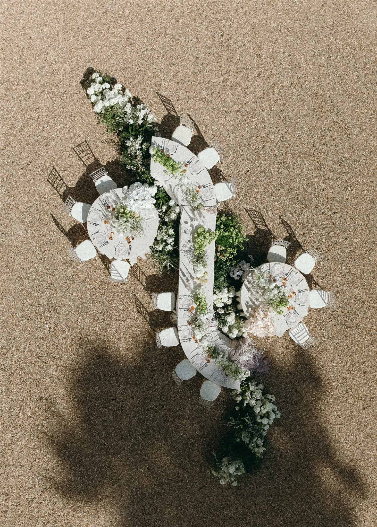 Aerial view of outdoor reception with one long and two round tables, continuous white floral runner with greenery