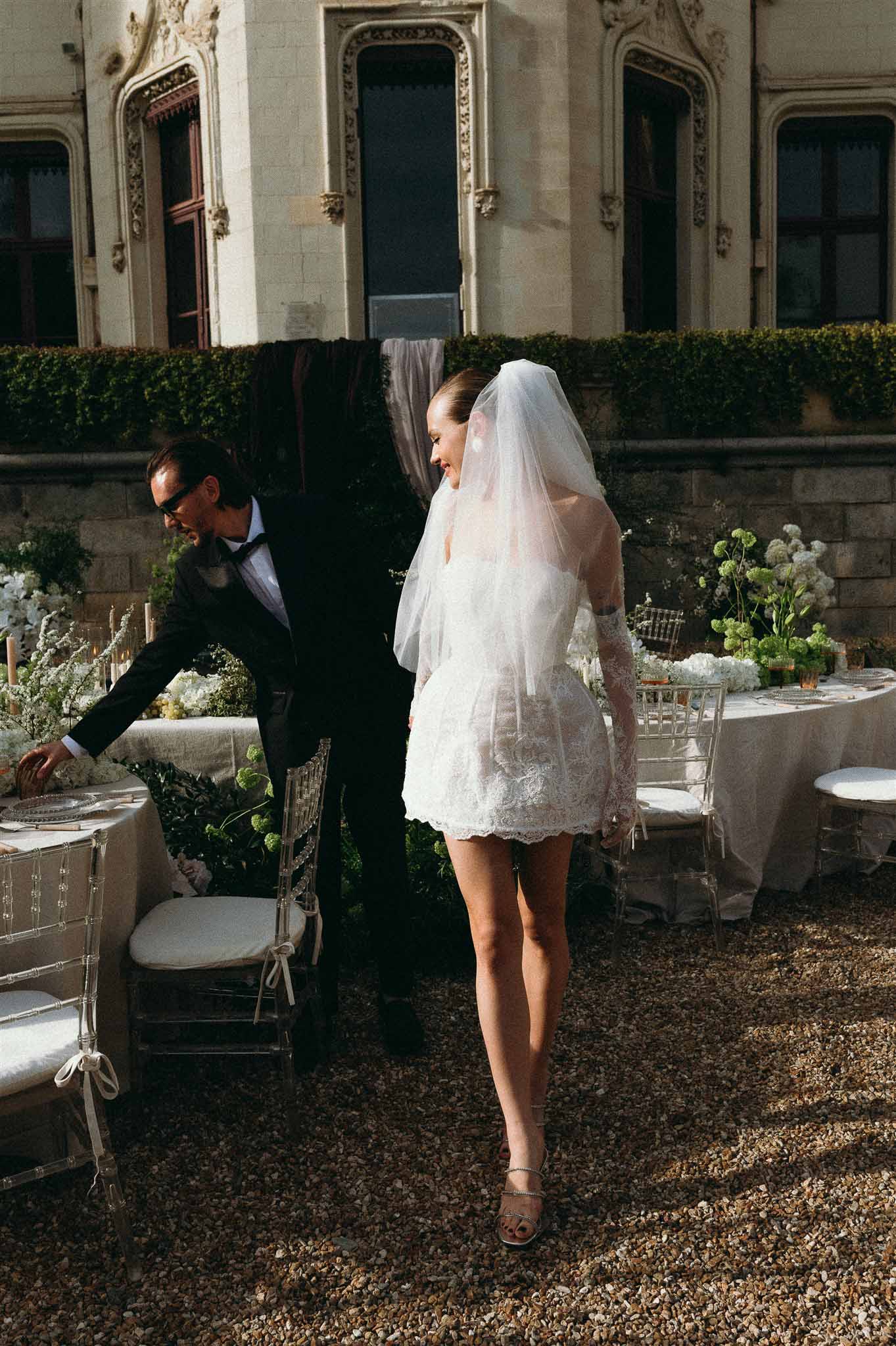 Bride in lace mini dress and groom in tuxedo at reception table with white hydrangea centerpieces