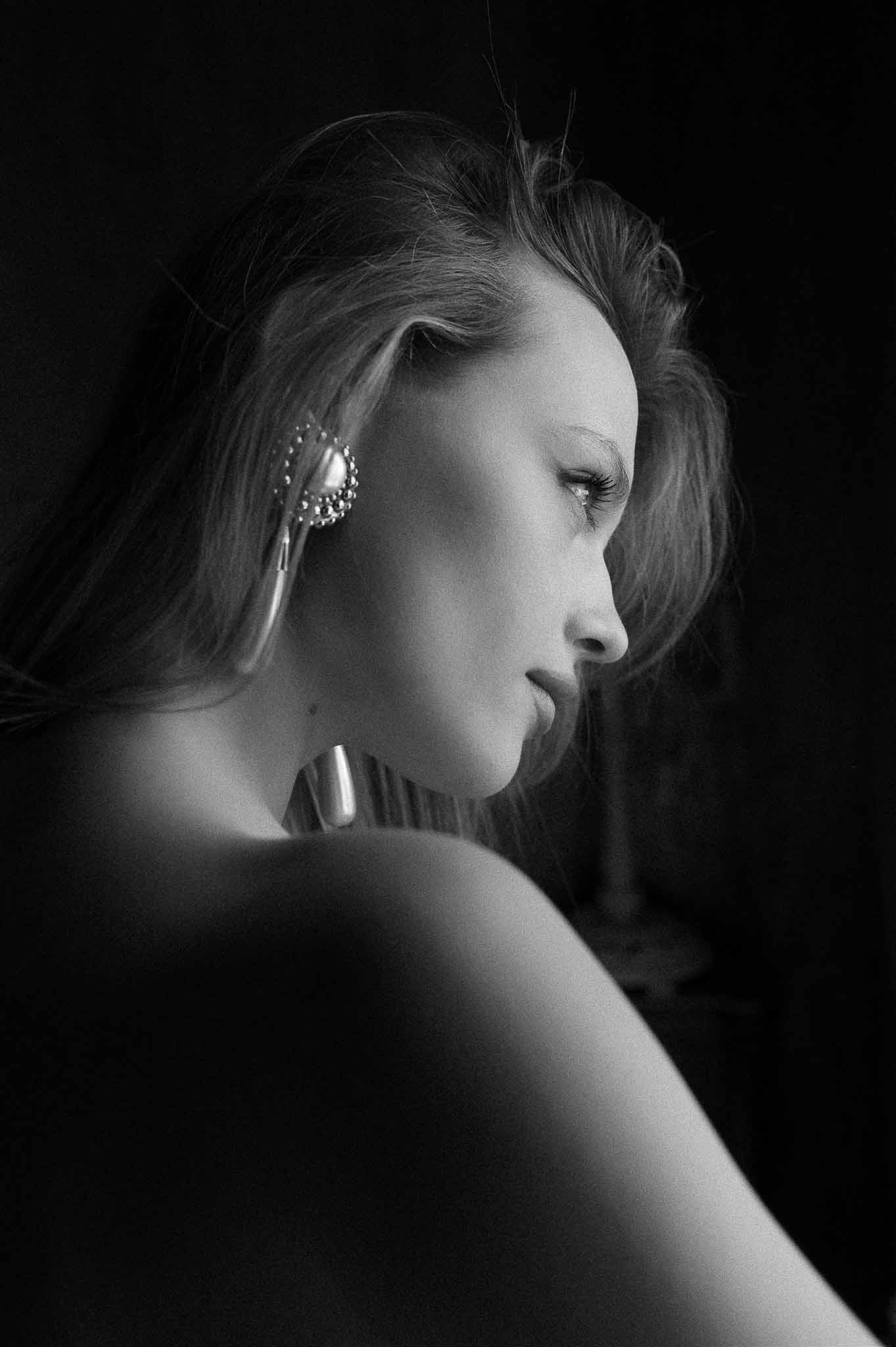 Black and white profile portrait of bride with statement embellished earrings and loose upswept hair in dramatic side ligh...