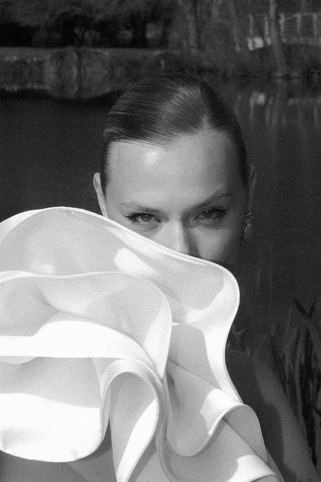 Black and white close-up of bride with slicked-back hair and drop earring, face framed by sculptural ruffle dress detail