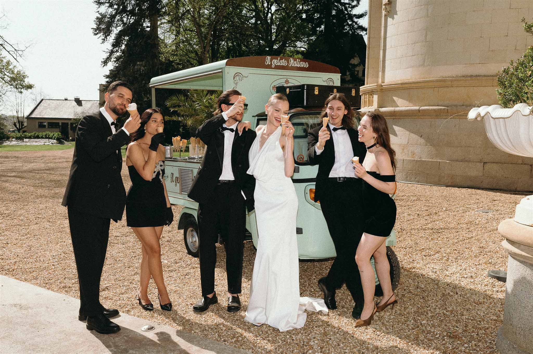 Bride and groom with four guests holding gelato cones before mint-green vintage Italian truck at chateau courtyard