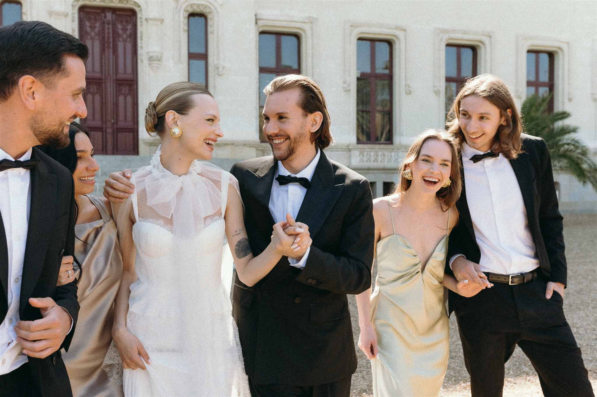 Bride and groom with two groomsmen and two bridesmaids in champagne and gold dresses laughing at chateau