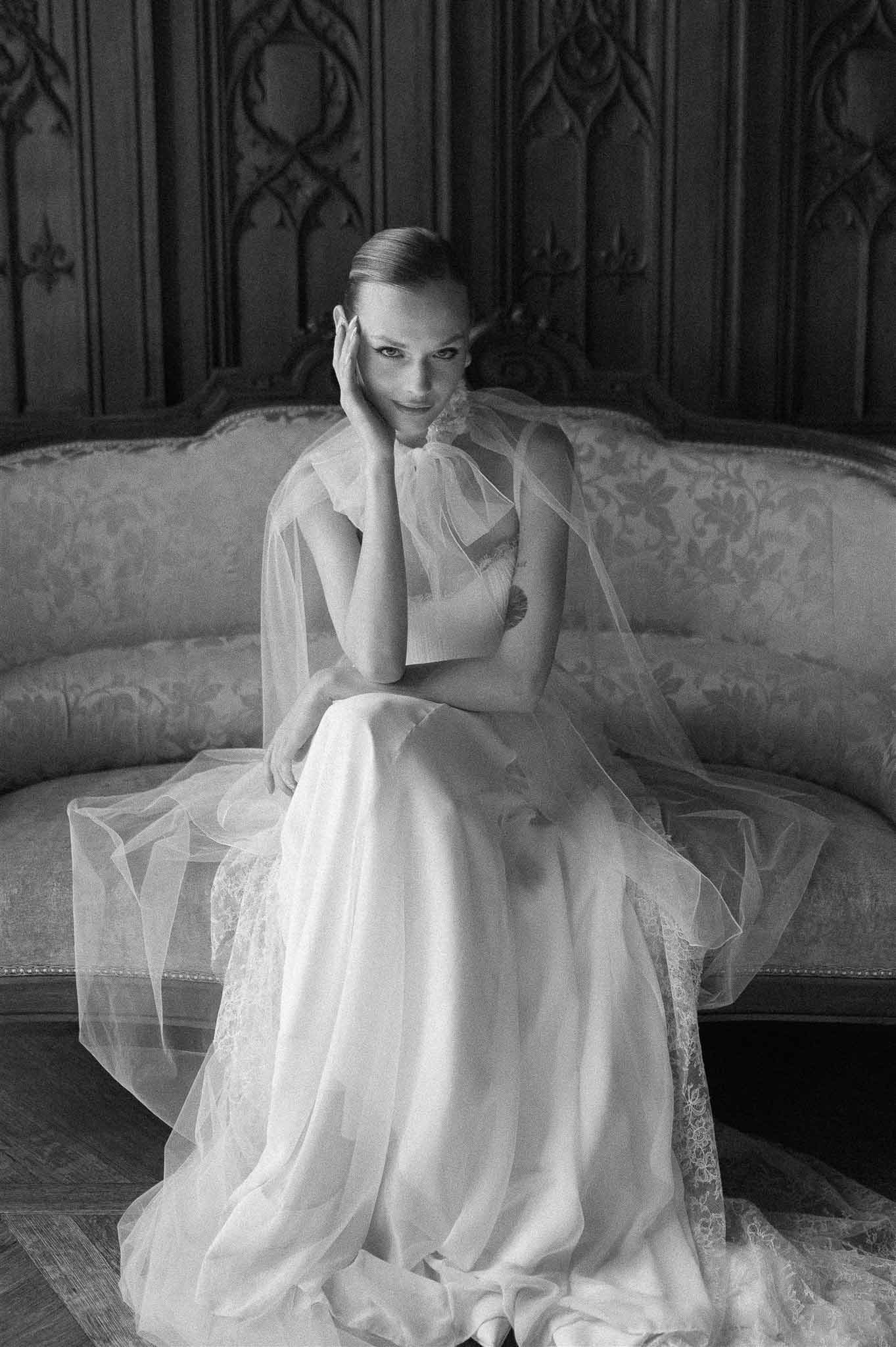 Bride in tulle gown with lace veil seated on damask settee in Gothic wood-paneled interior in B&W