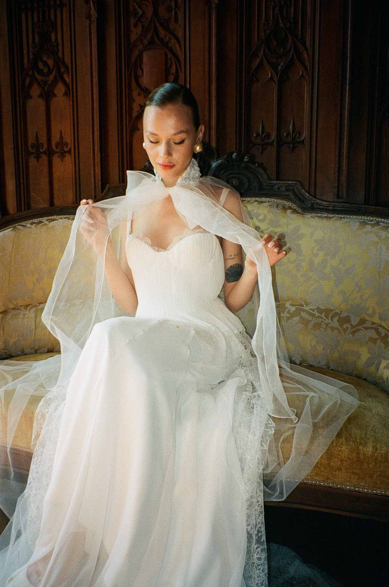 Bride holding lace veil on gold damask settee in chateau interior with Gothic wood paneling