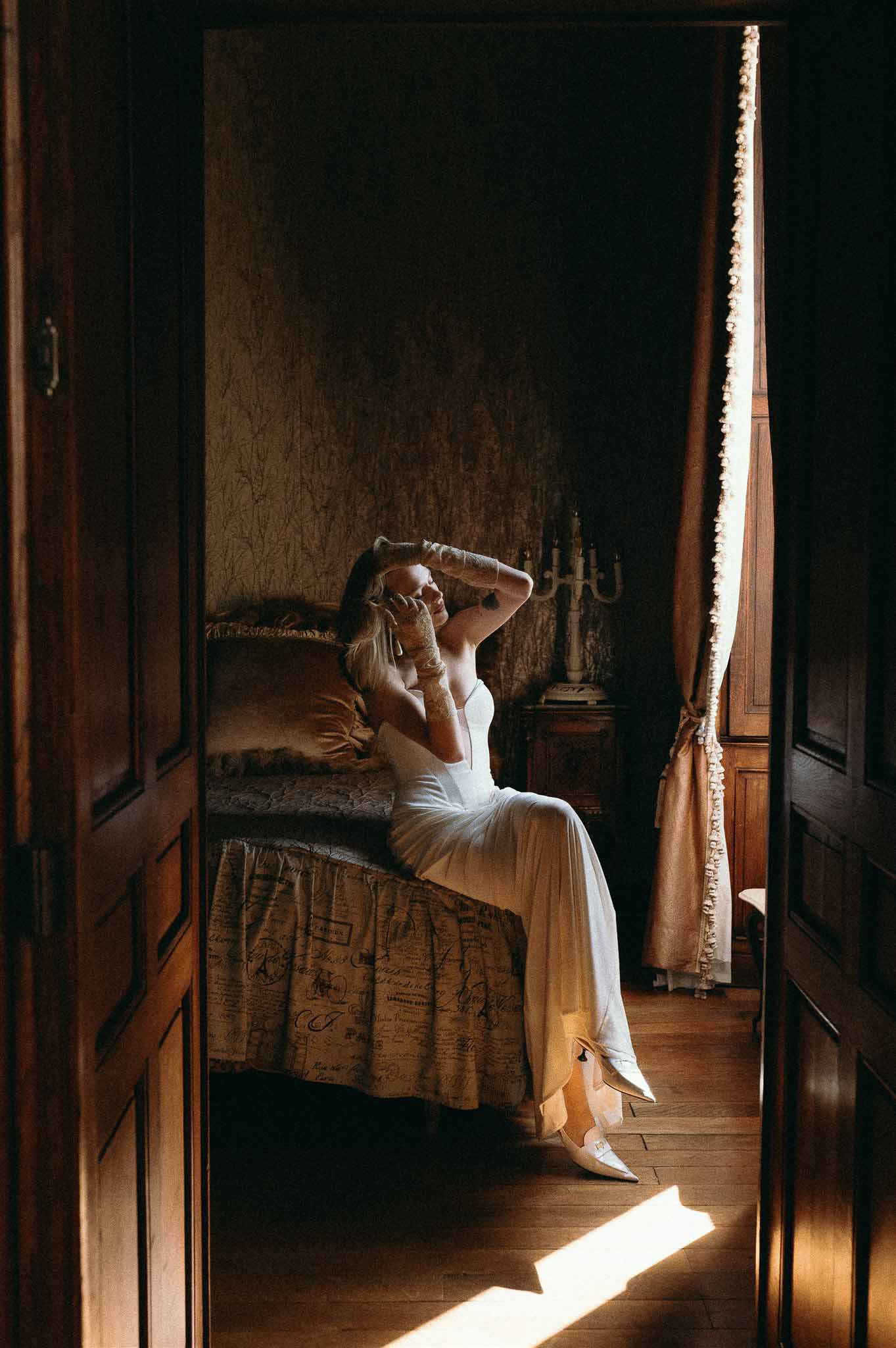 Bride in slip gown with lace gloves framed through doorway in candlelit chateau bedroom