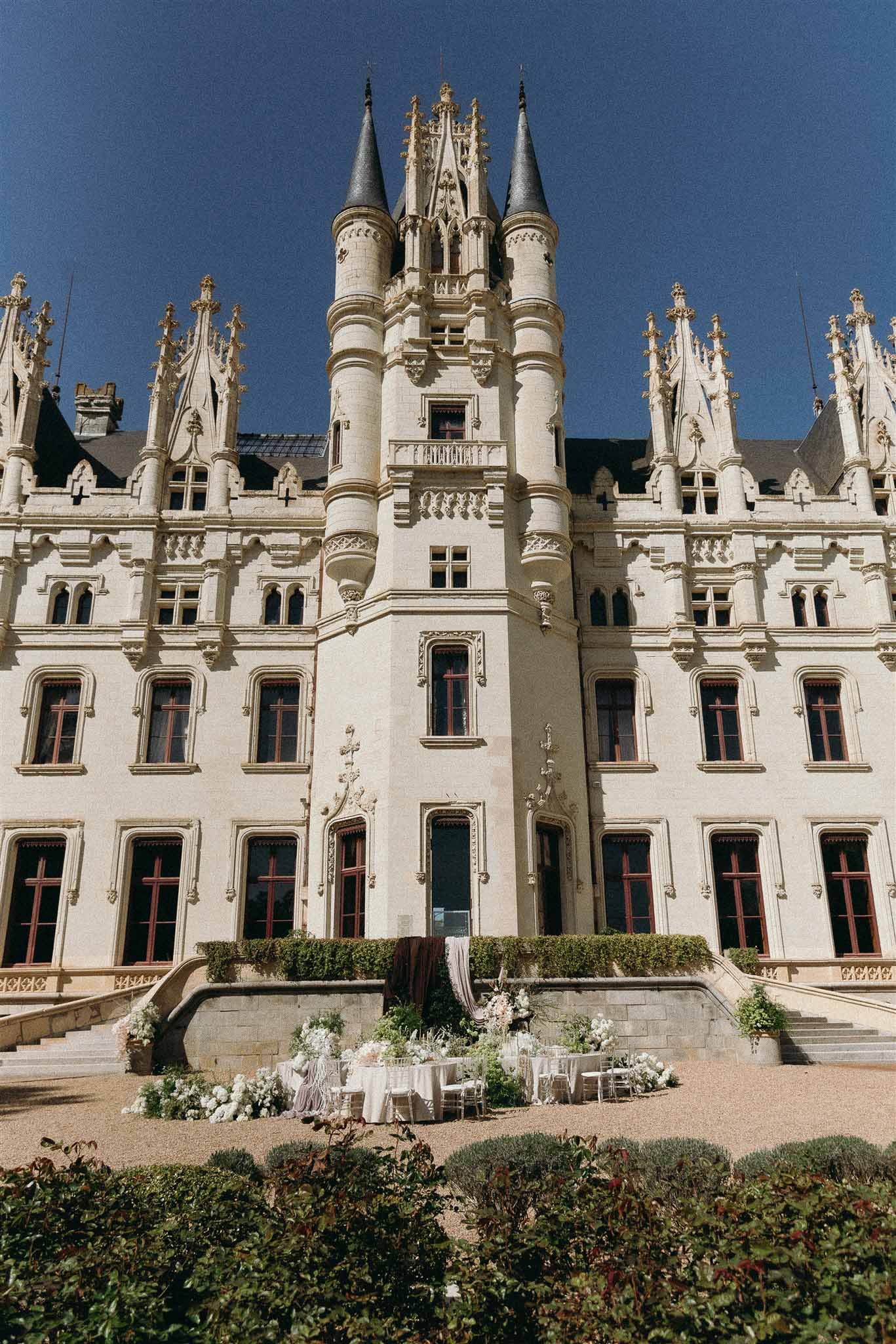Gothic chateau with limestone facade and slate turrets with reception table and floral arrangements in courtyard