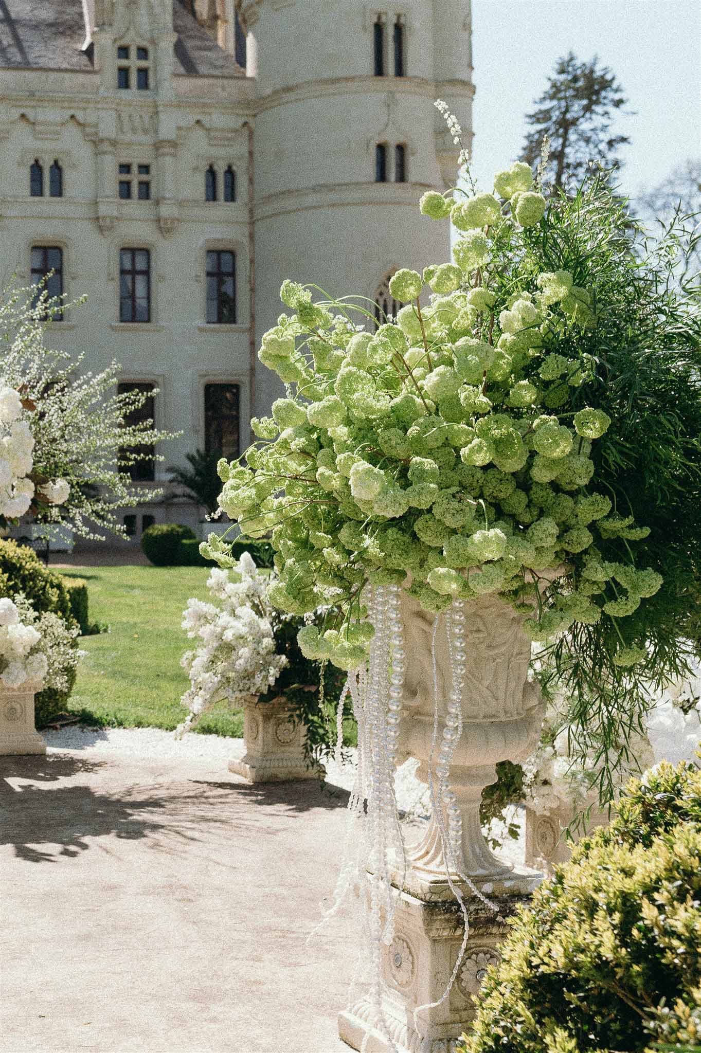 Stone urn with green viburnum blooms and trailing crystal garlands on a chateau pathway
