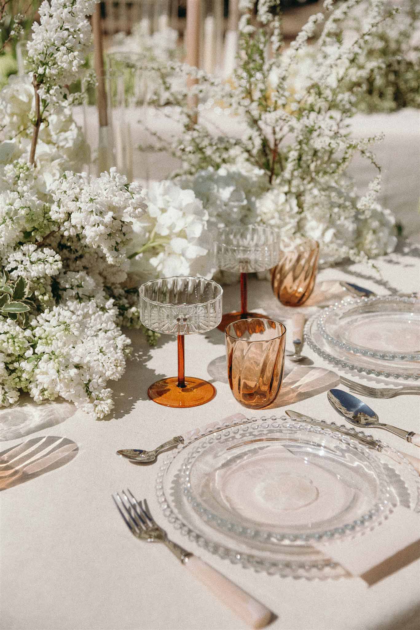 All-white hydrangea and lilac centerpiece with amber stemware and beaded glass charger plates