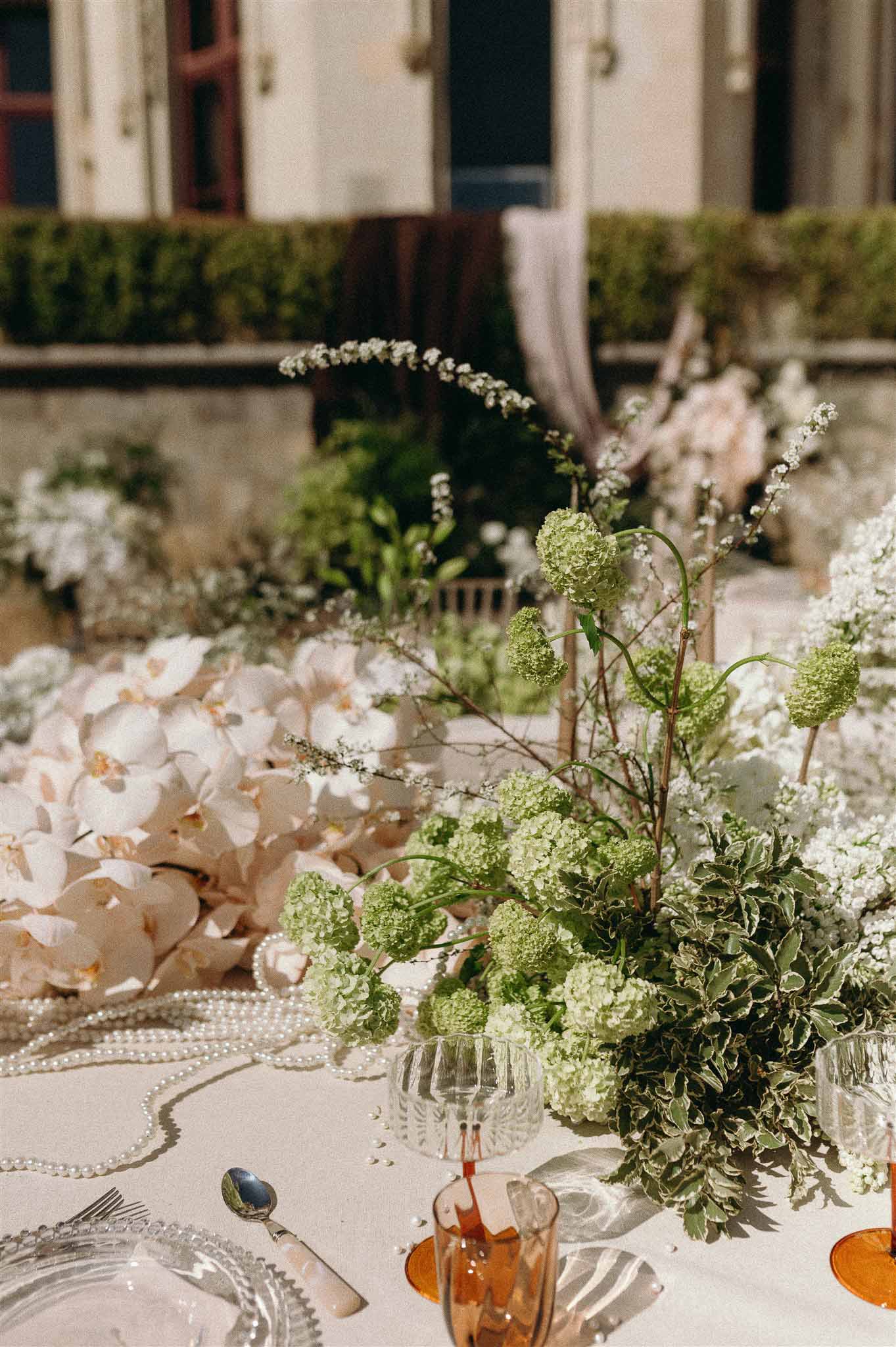 Centerpiece of blush orchids chartreuse viburnum and spirea with pearl strands and amber glassware
