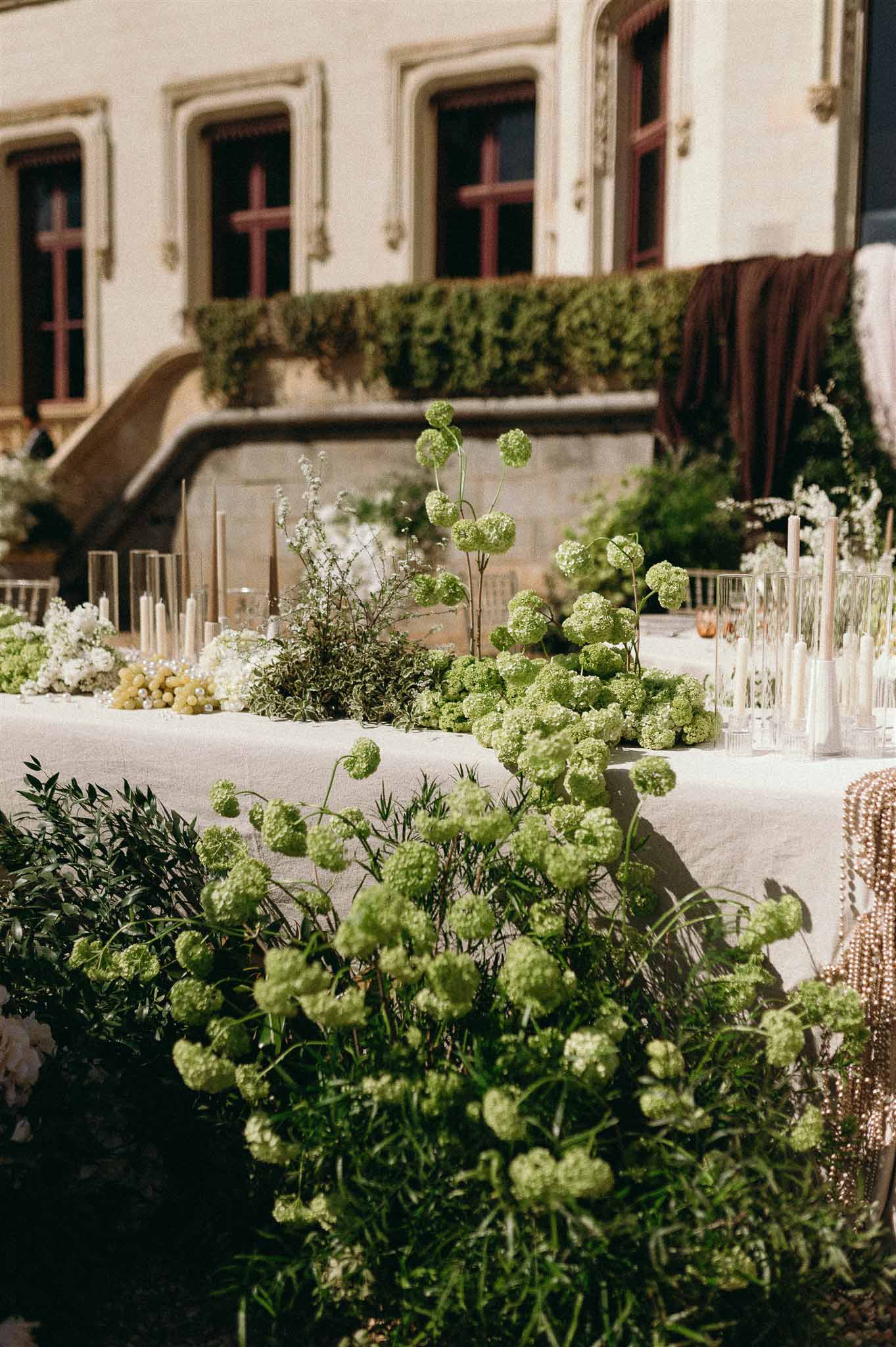 Floral runner with chartreuse viburnum white gypsophila ivory candles in hurricanes and green grapes on white linen