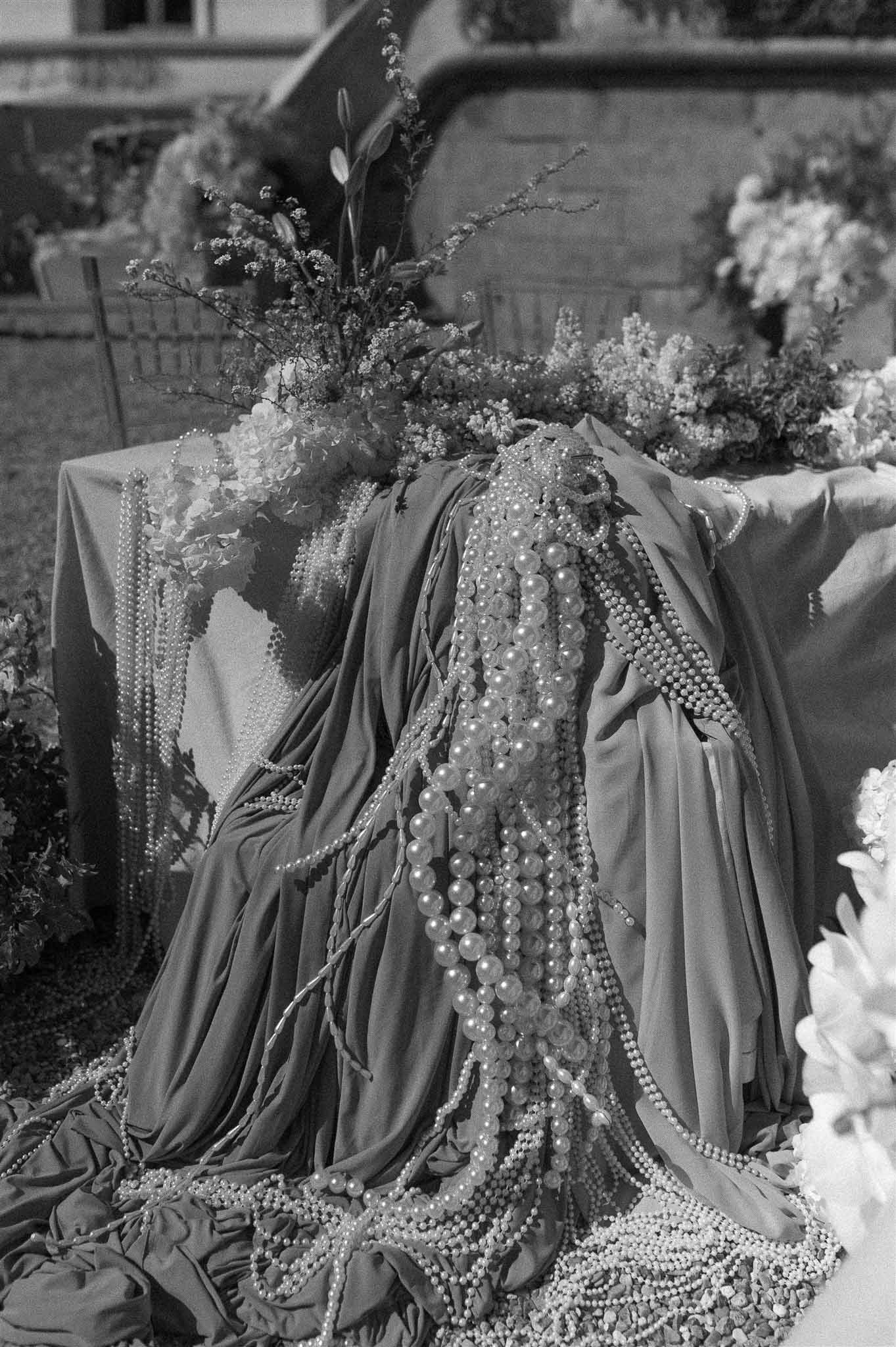 Black and white cascading pearl strands and lily arrangement on draped fabric with stone backdrop