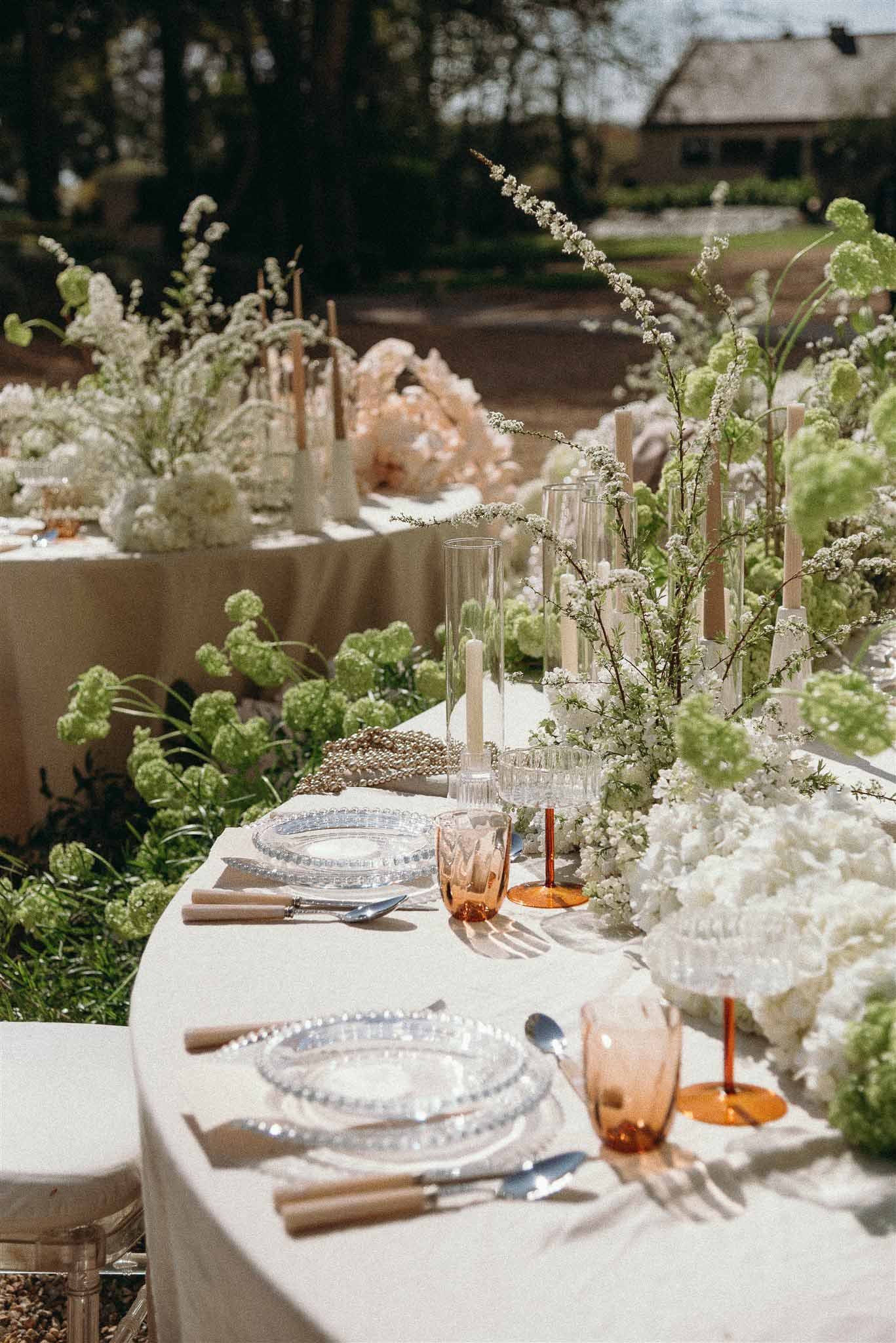 Reception table with white hydrangeas, viburnum, pearl strands, and amber glass hurricane candles