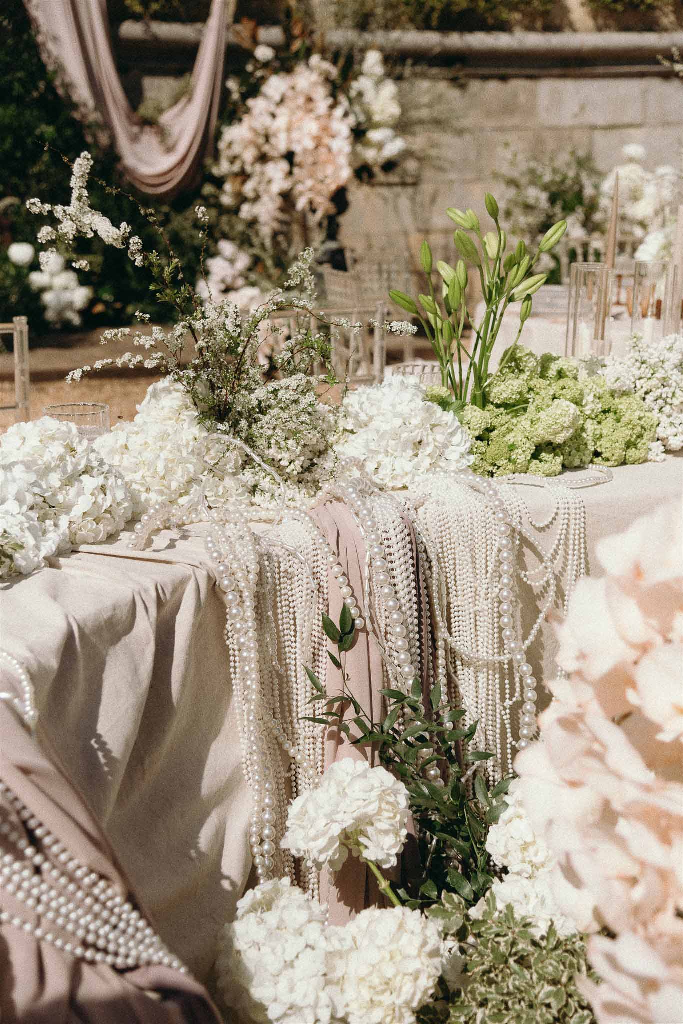 Reception table with pearl bead chain draping white hydrangea cherry blossom runner and ghost chairs