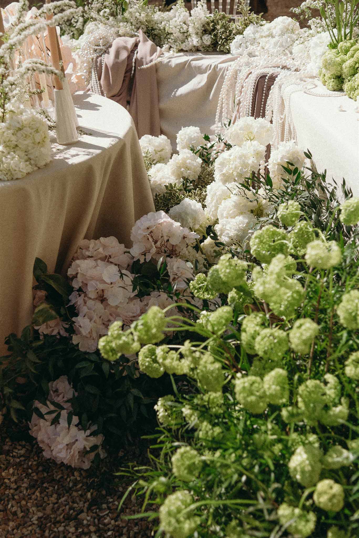 Reception table with pearl-draped chairs, white peonies, blush hydrangeas, and champagne linens