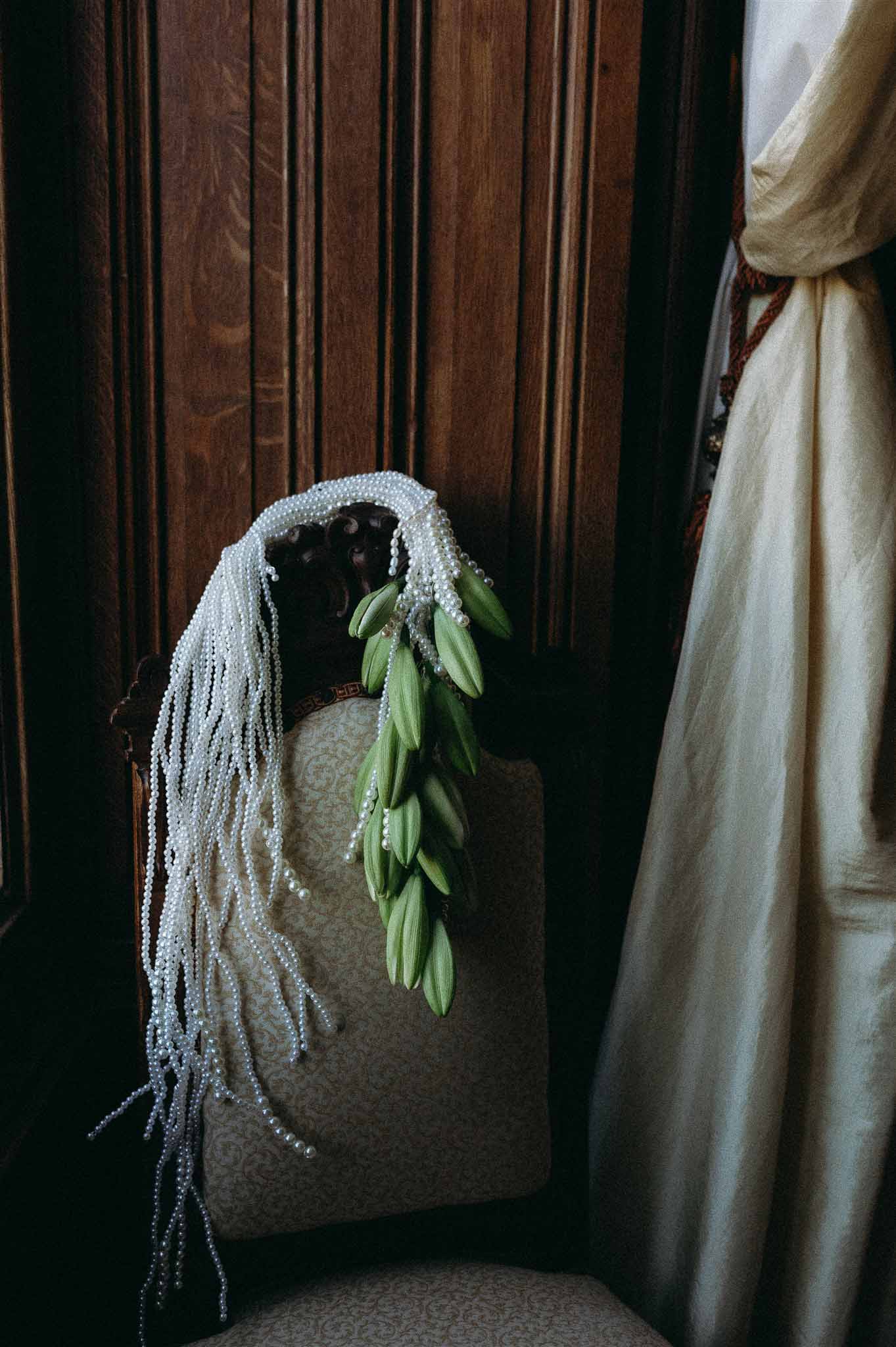 Pearl and lily of the valley cascading bridal headpiece draped over antique carved chair