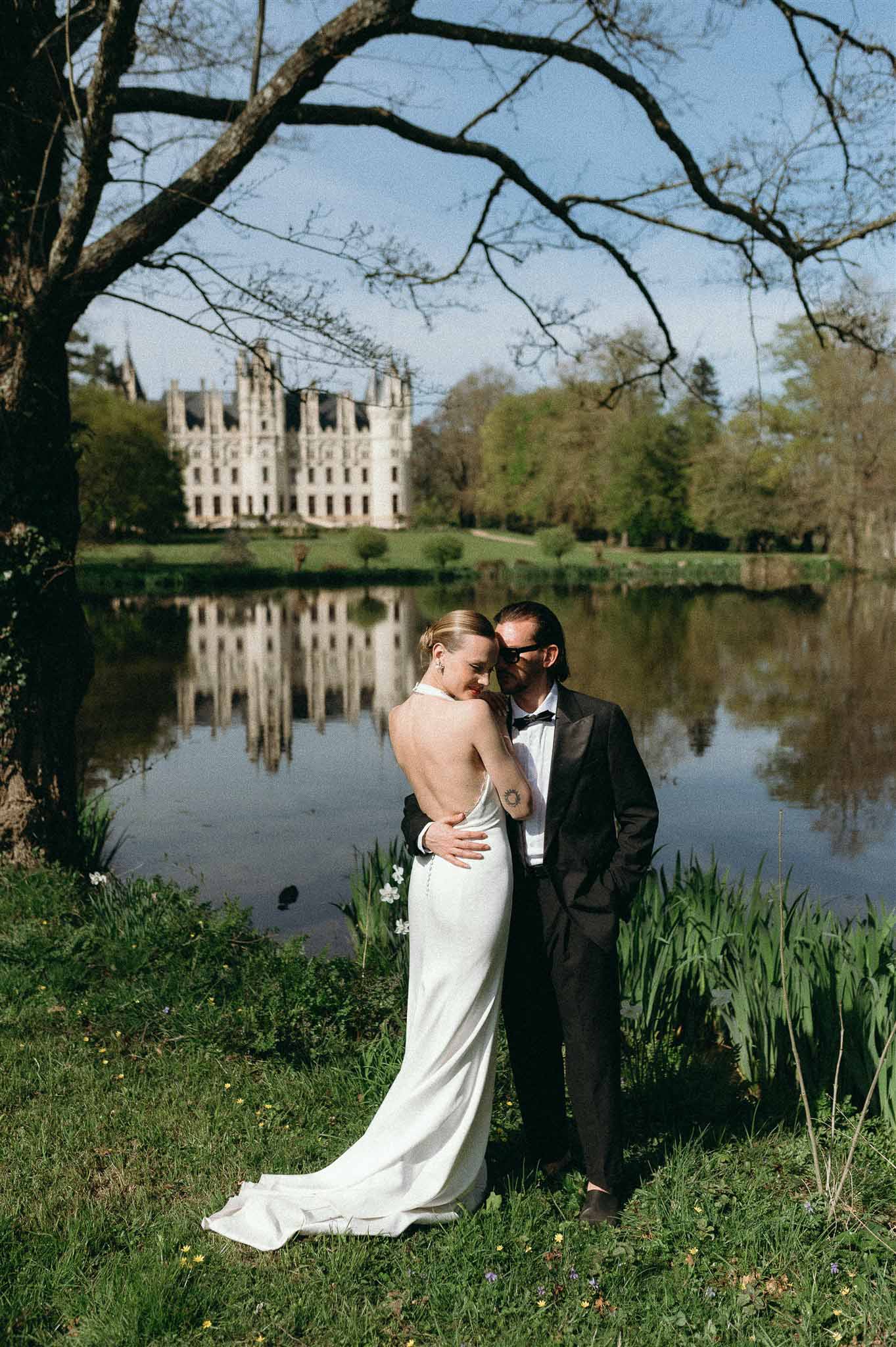 Bride and groom standing by a reflective pond with a Renaissance chateau reflected in the water behind them