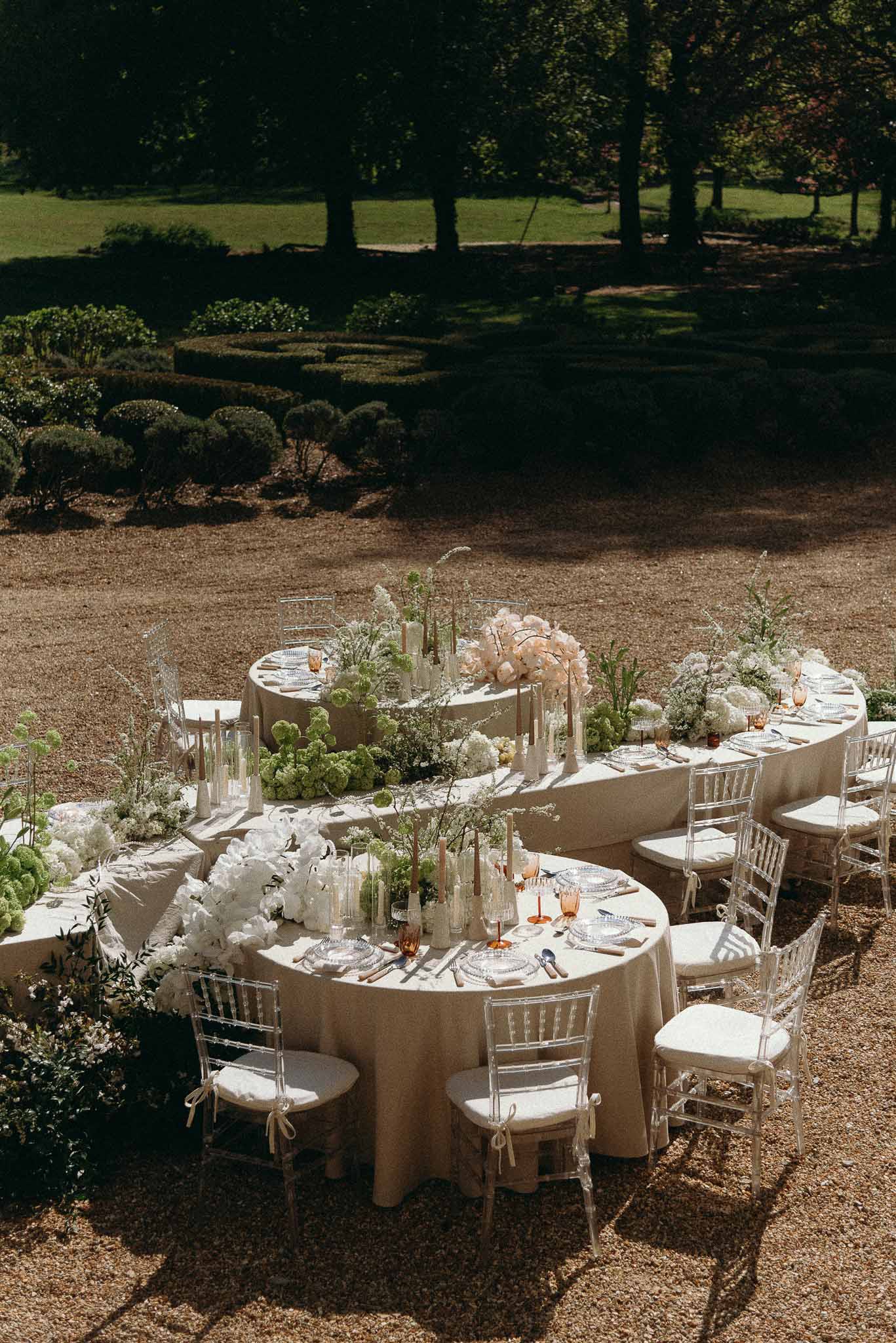 Serpentine round tables with acrylic chairs, viburnum and peony runner in formal hedged garden