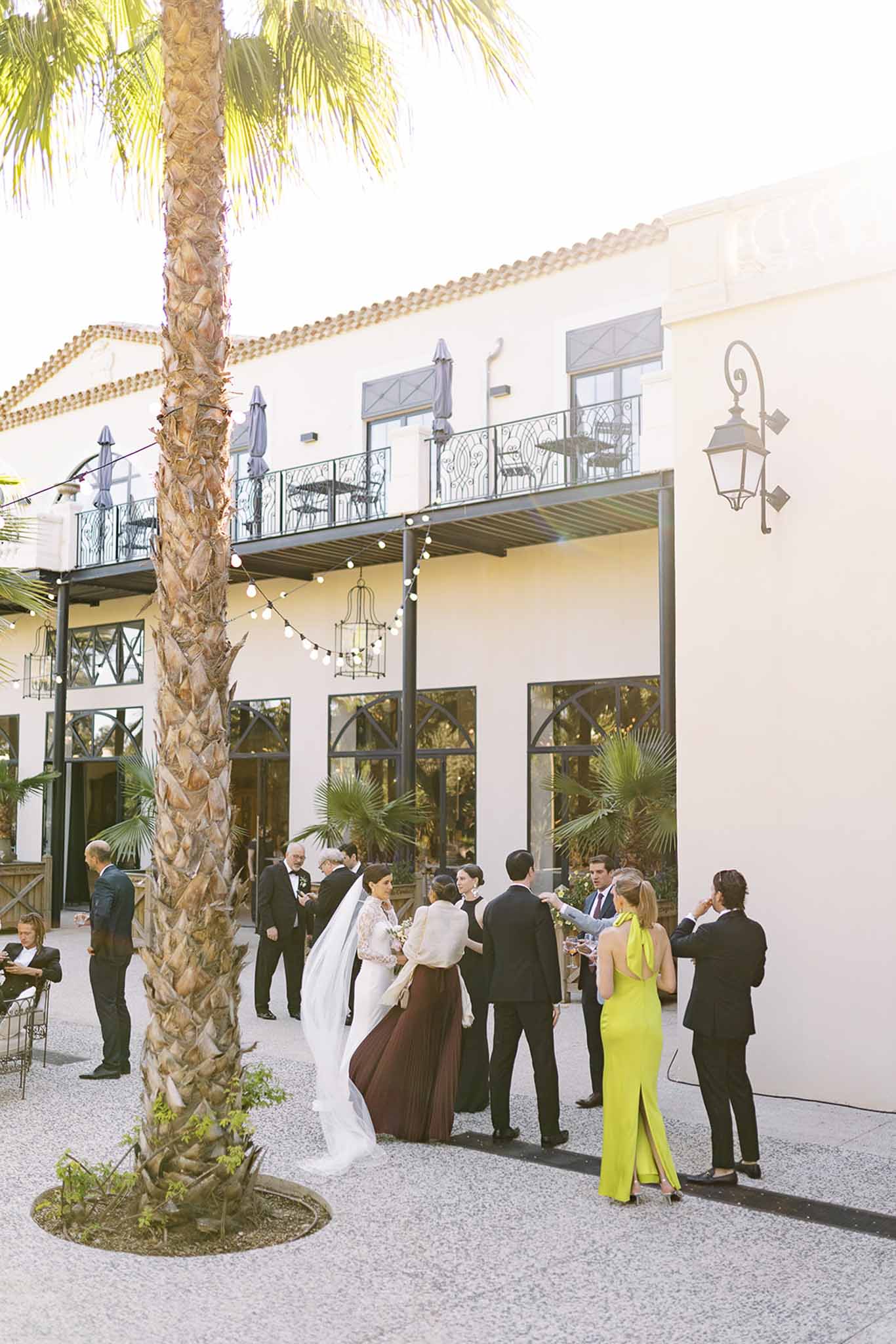 Guests mingling on courtyard at golden hour before Mediterranean venue with terracotta roof and string lights