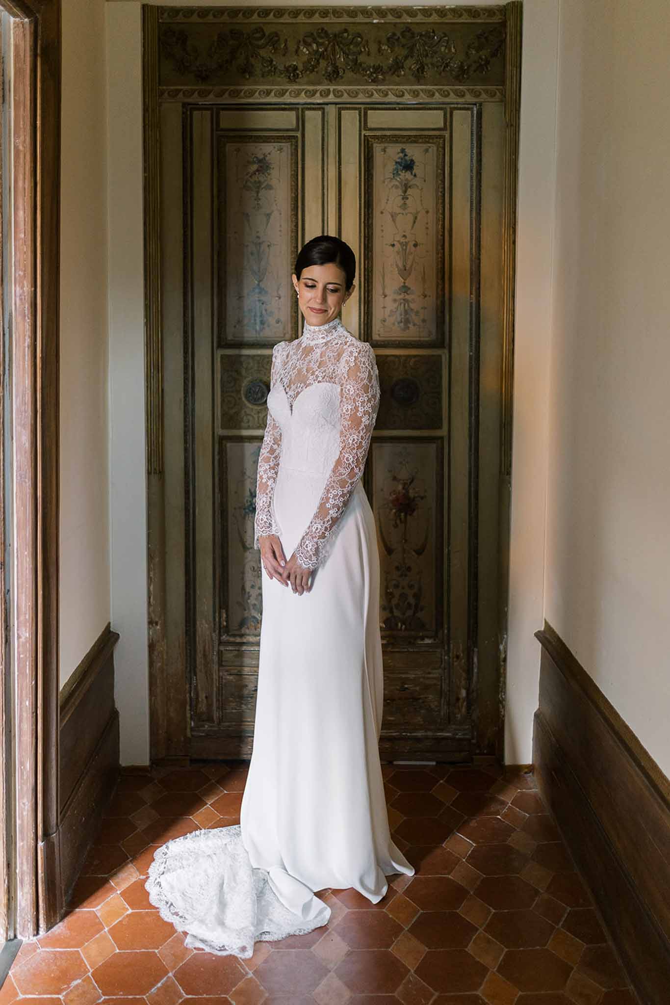 Bride in high-neck lace gown with sheer sleeves and crepe train before painted chateau doors
