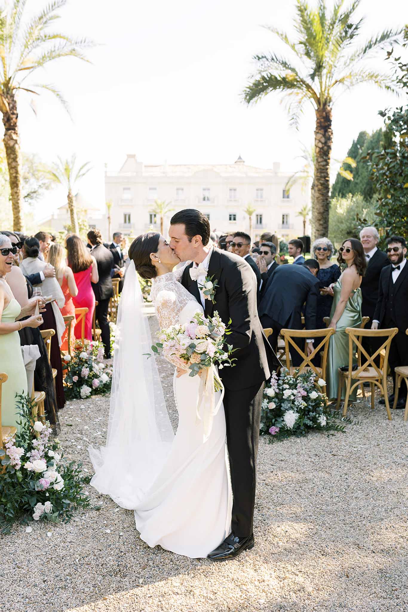 First kiss on lawn aisle lined with blush roses as 40 guests applaud before white mansion