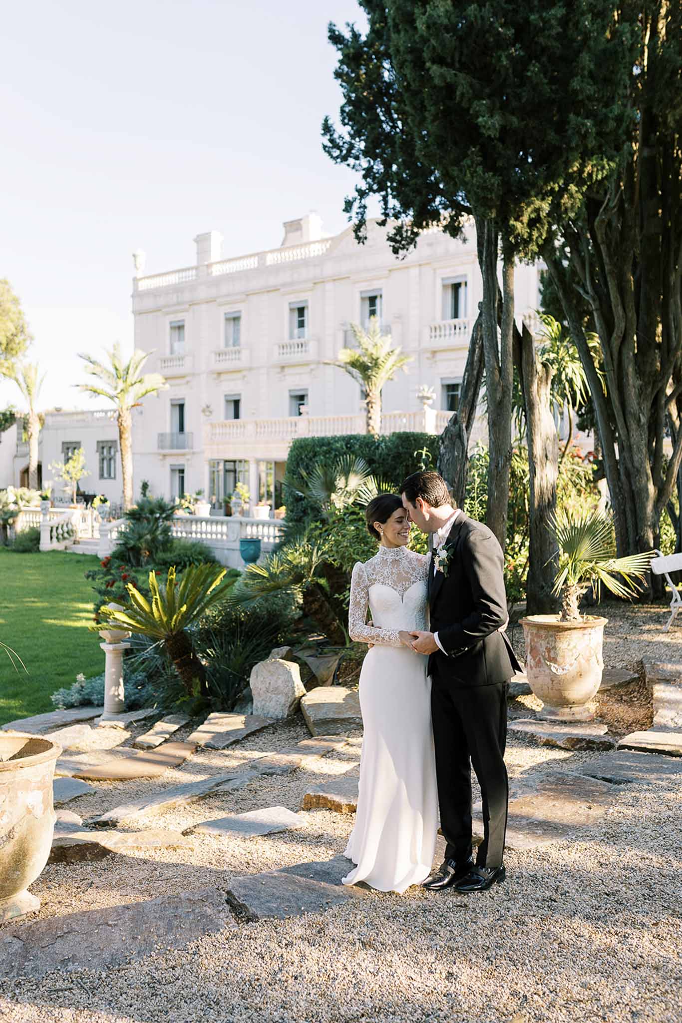 Couple touching foreheads on stone terrace with palm trees and white villa balustrade behind