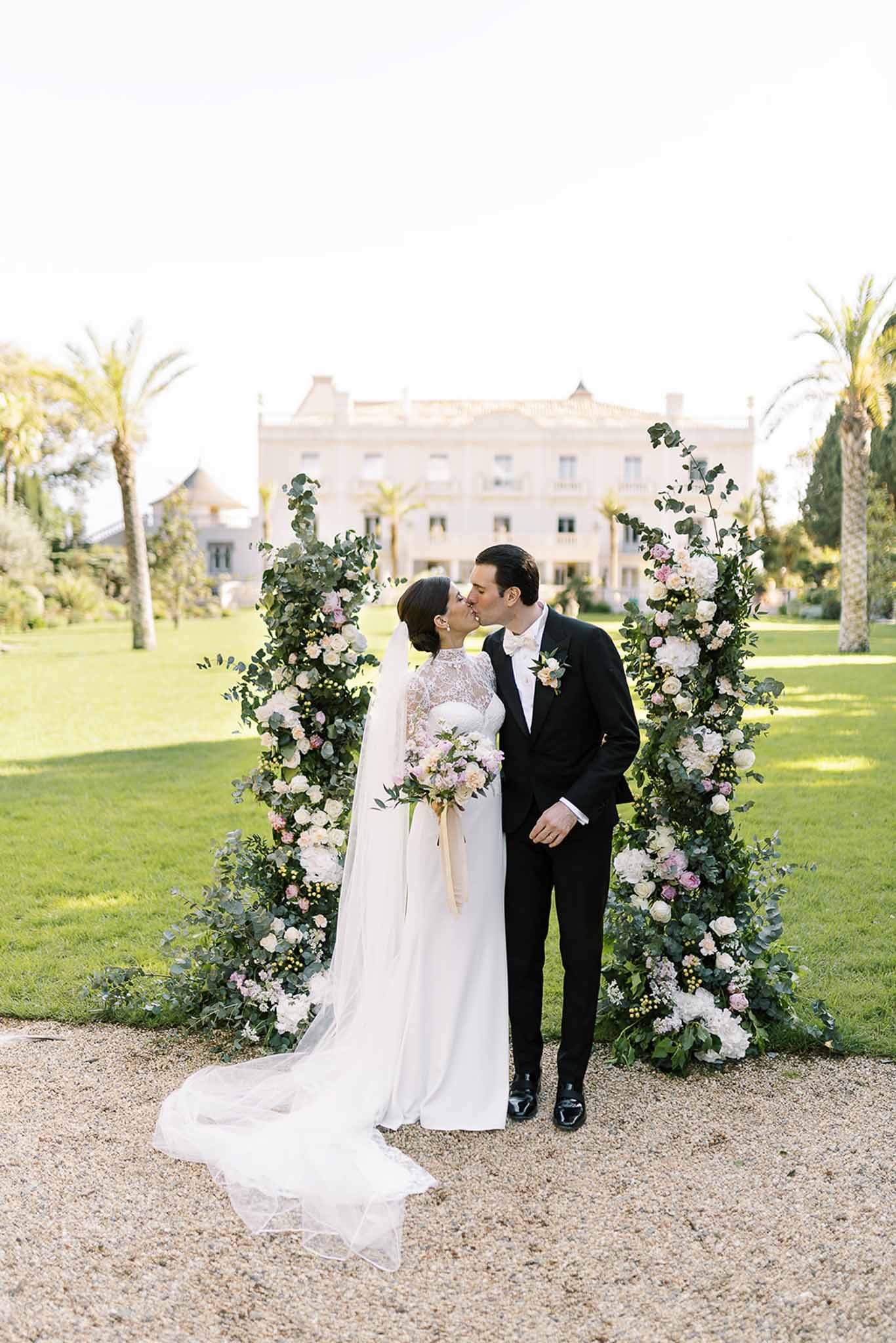 Couple kissing before tall floral columns of roses and hydrangeas at manor entrance