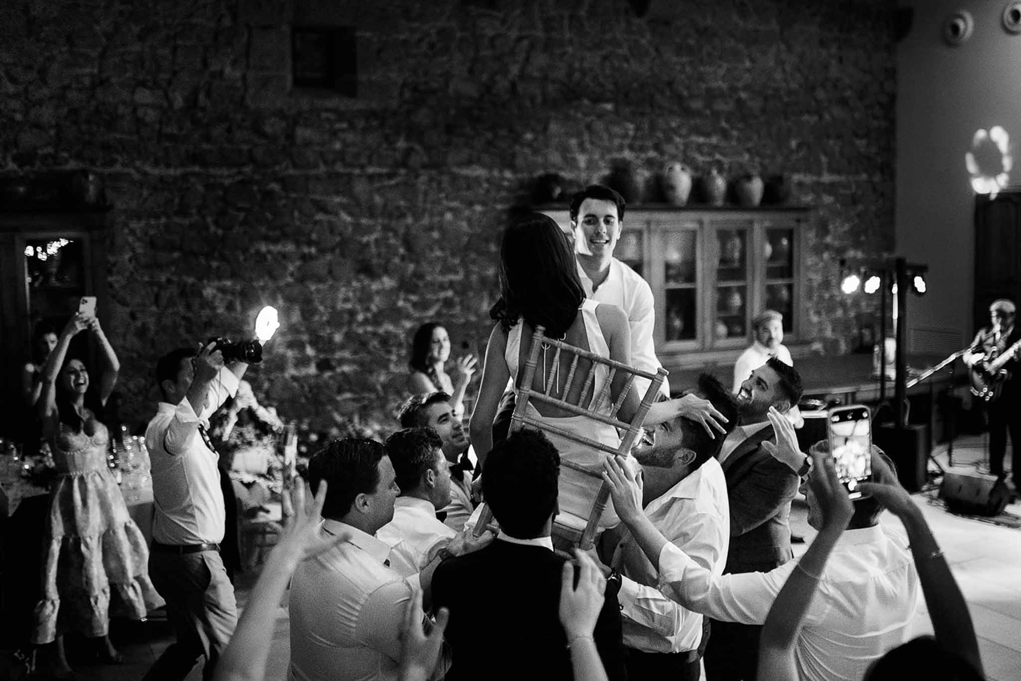Black and white Hora chair dance with couple lifted by guests at indoor reception