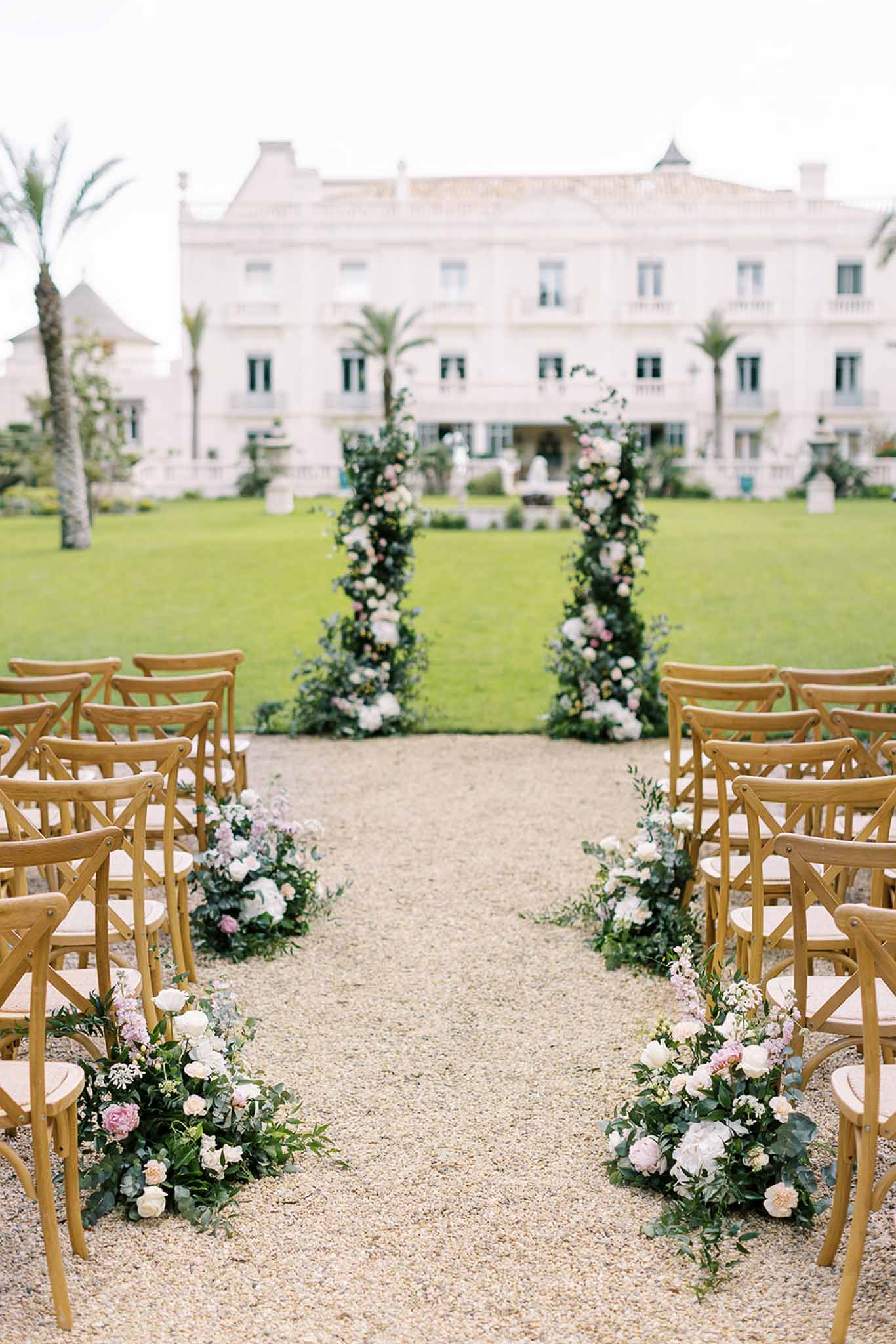 Ceremony aisle with spiral floral columns and blush aisle arrangements before white neoclassical manor