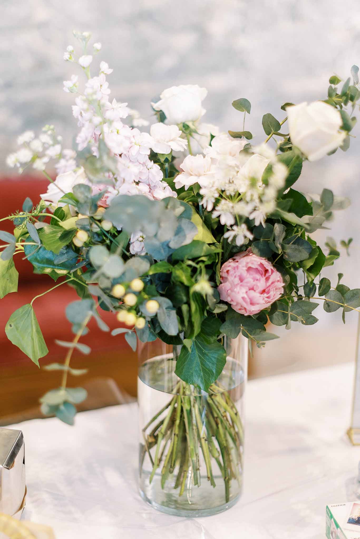Glass vase centerpiece with pink peony white roses blush stock and eucalyptus on white linen table