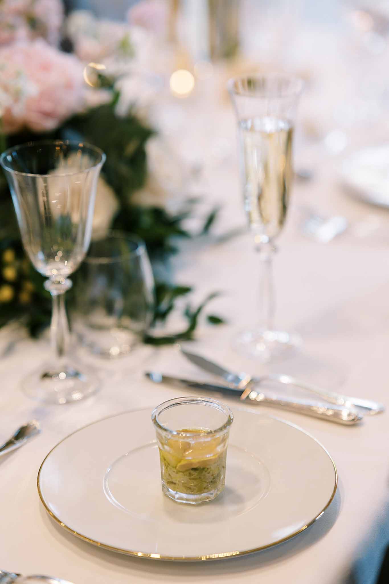 Gold-rimmed charger with amuse-bouche, crystal flutes, and blush rose centrepiece on white linen