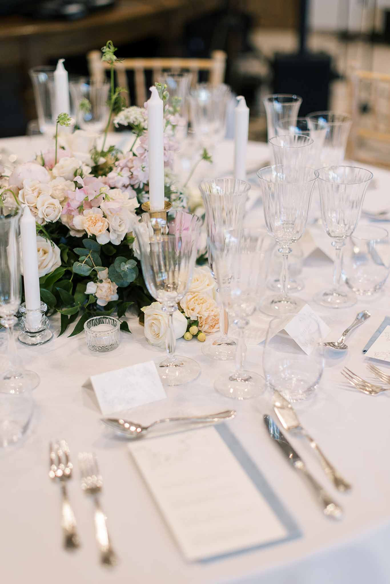 Reception table detail with cream roses, blush sweet peas, crystal glassware, and white taper candles