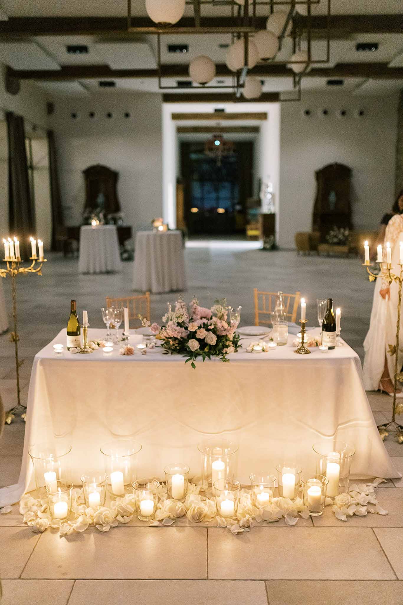 Sweetheart table with blush roses, gold candelabras, and floor candles in candlelit ballroom