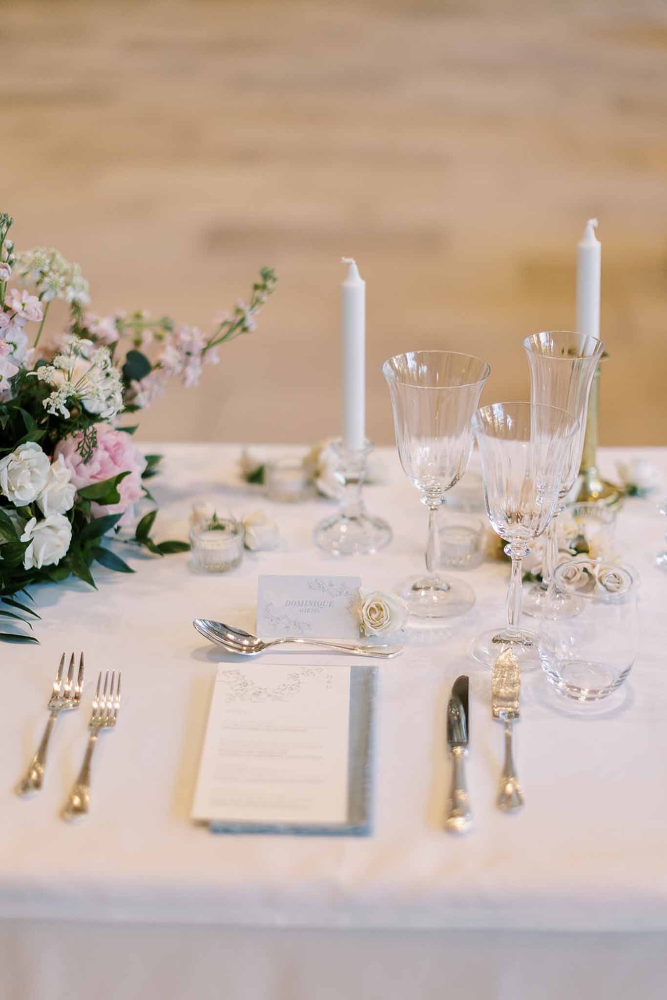 Wedding reception place setting with printed menu card, silver cutlery, crystal glasses, and blush peonies