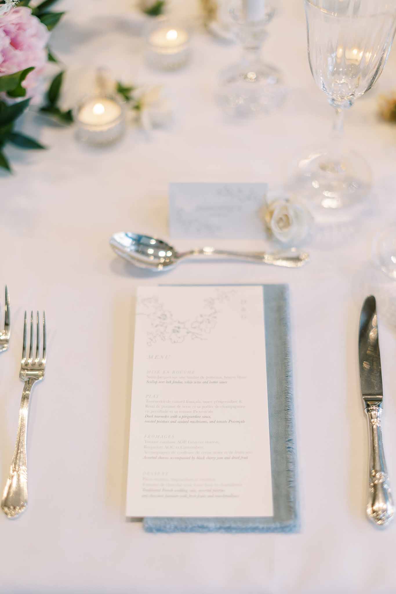 Place setting with printed menu dusty blue napkin silver cutlery white rose and blush peony centerpiece