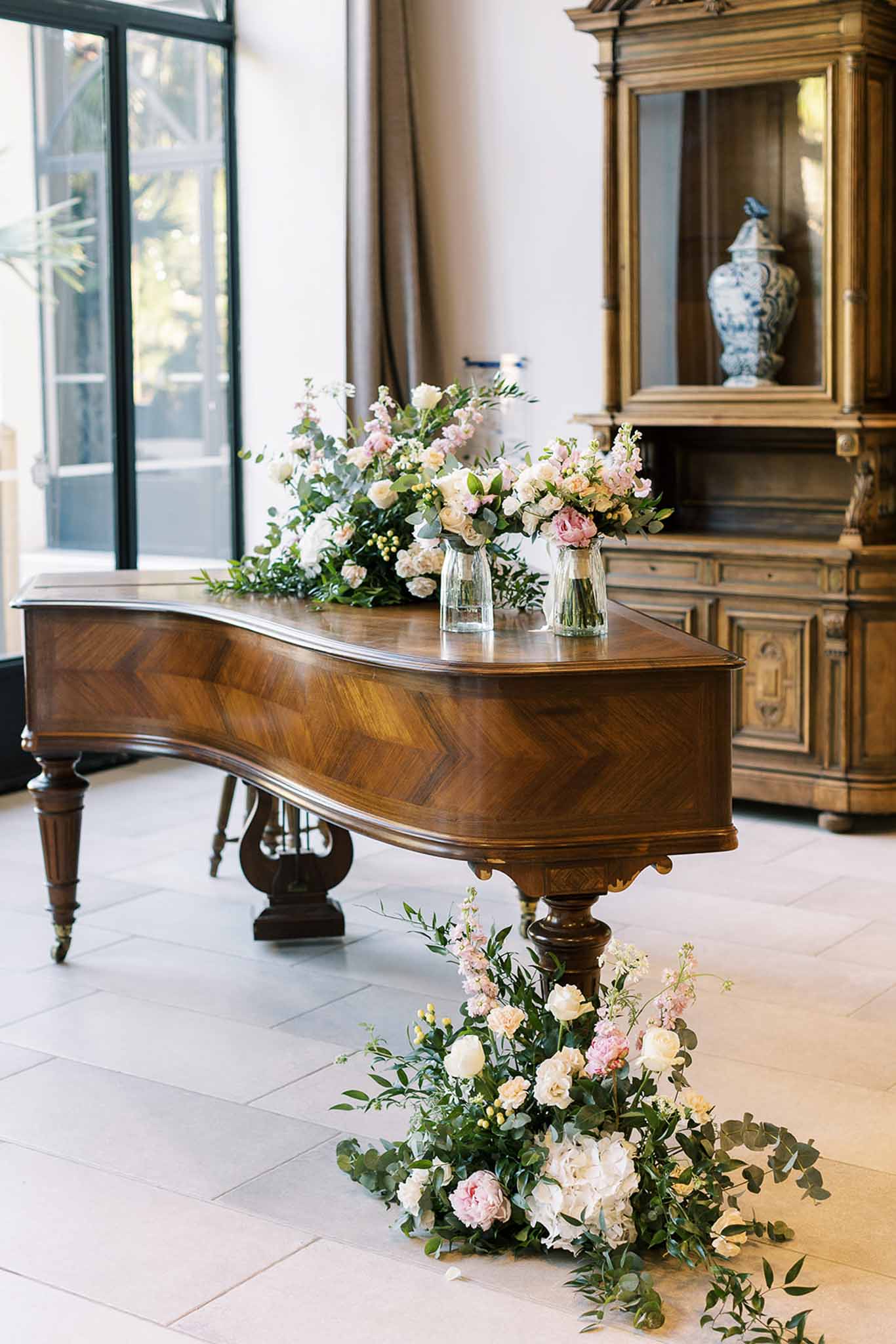 Walnut grand piano with blush rose arrangements and floor-level peony installation beside Delft vase