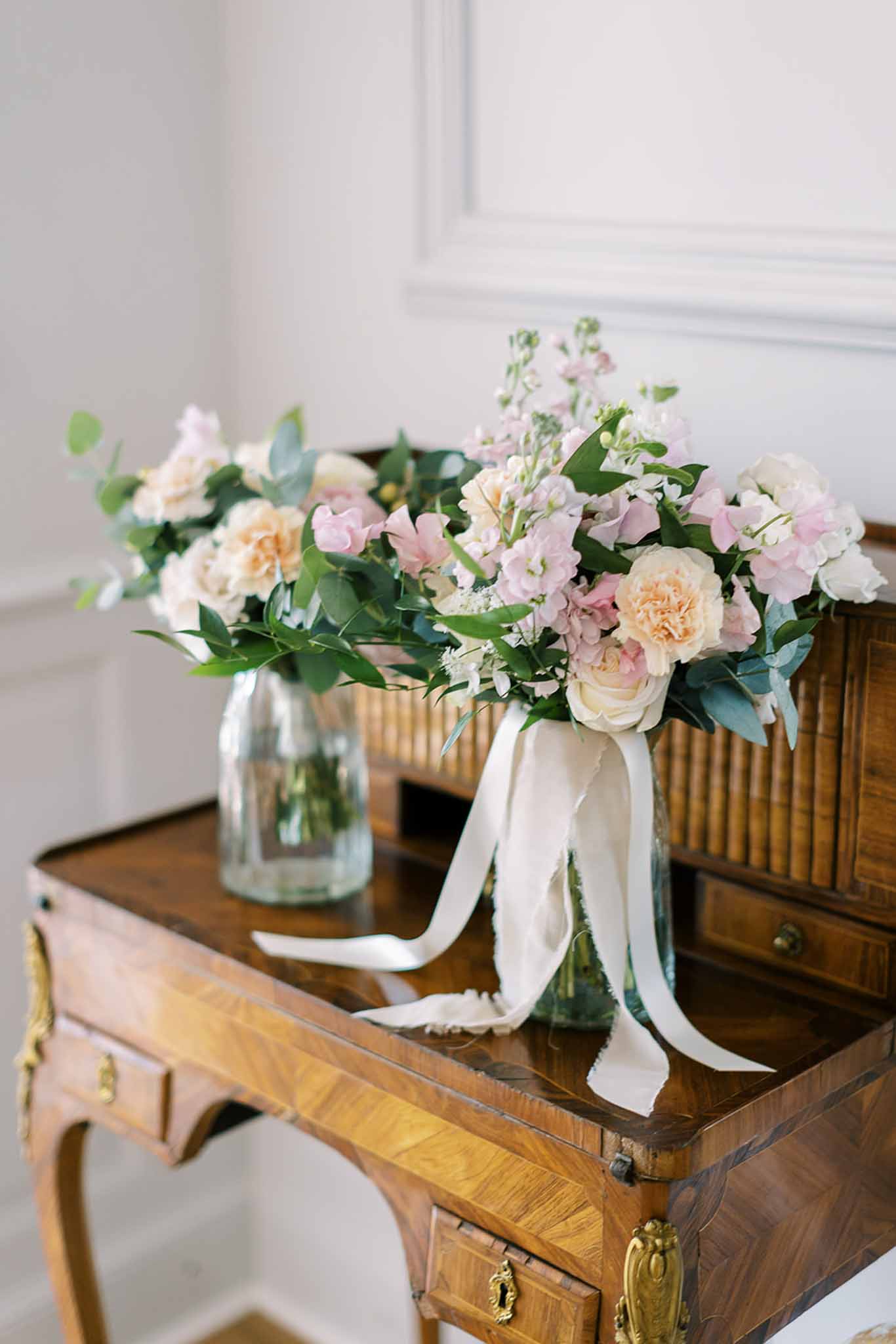 Bridal bouquet of blush sweet peas, peach roses, and cream carnations with silk ribbons on antique writing desk