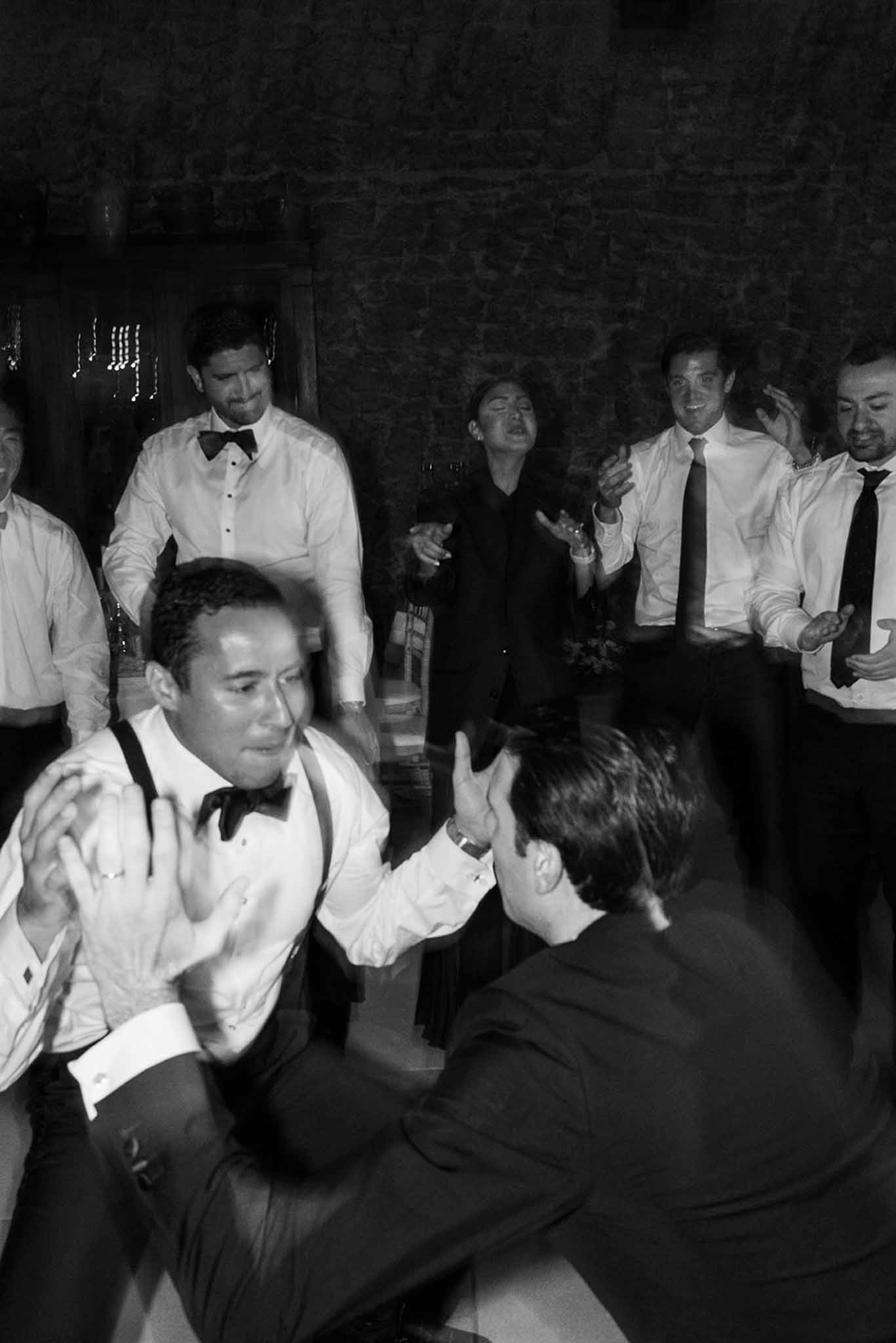 Black-and-white photo of energetic reception dancing inside stone-walled venue with guests cheering