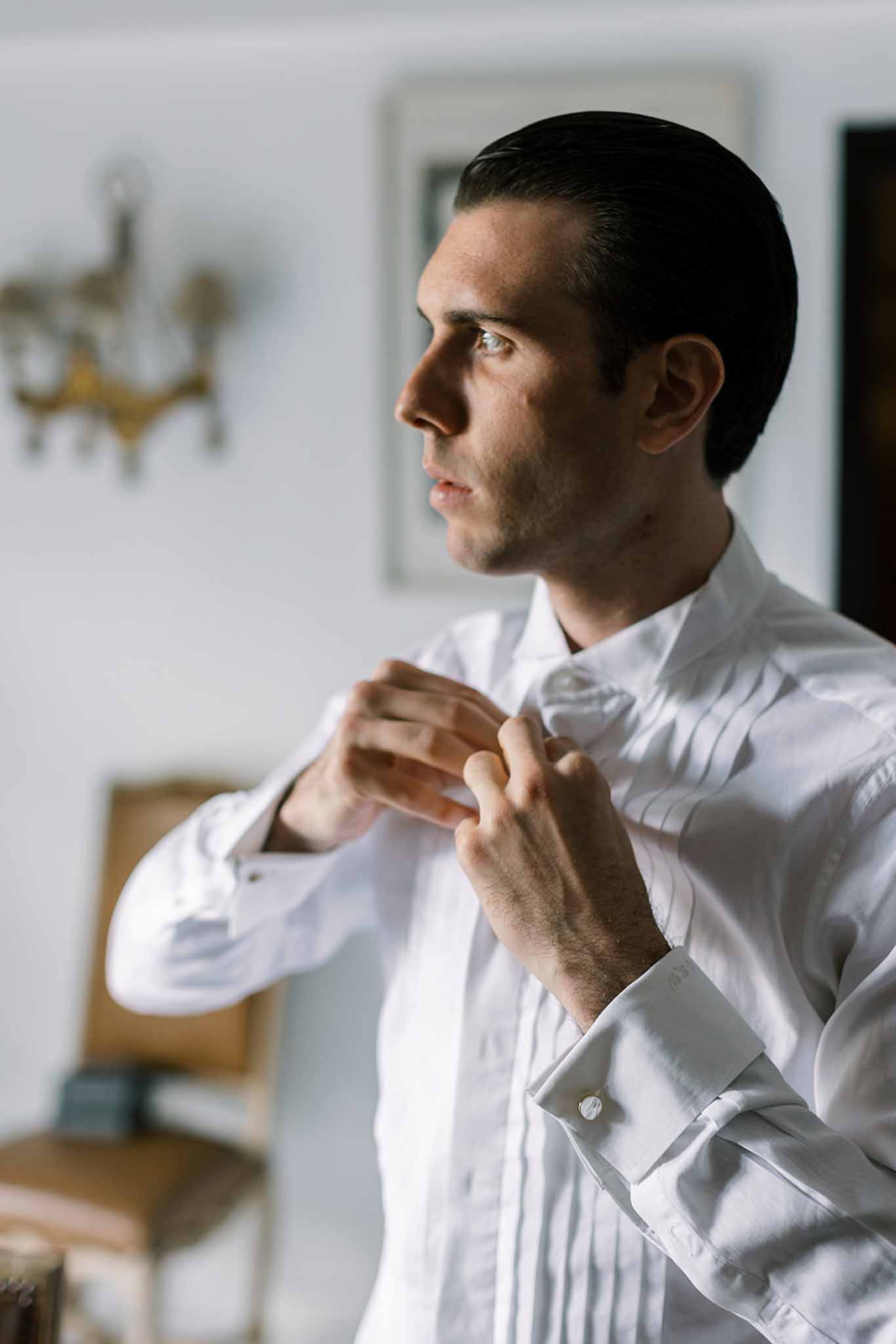 Groom fastens grey bow tie on pleated dress shirt with silver cufflinks in close-up portrait