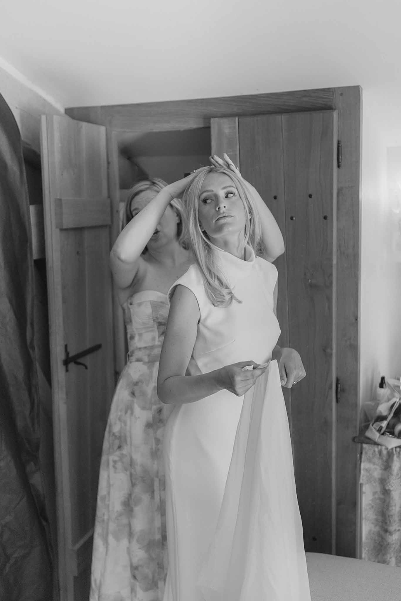 Black and white companion securing brides hair in rustic room with wooden doors bride in sleeveless gown