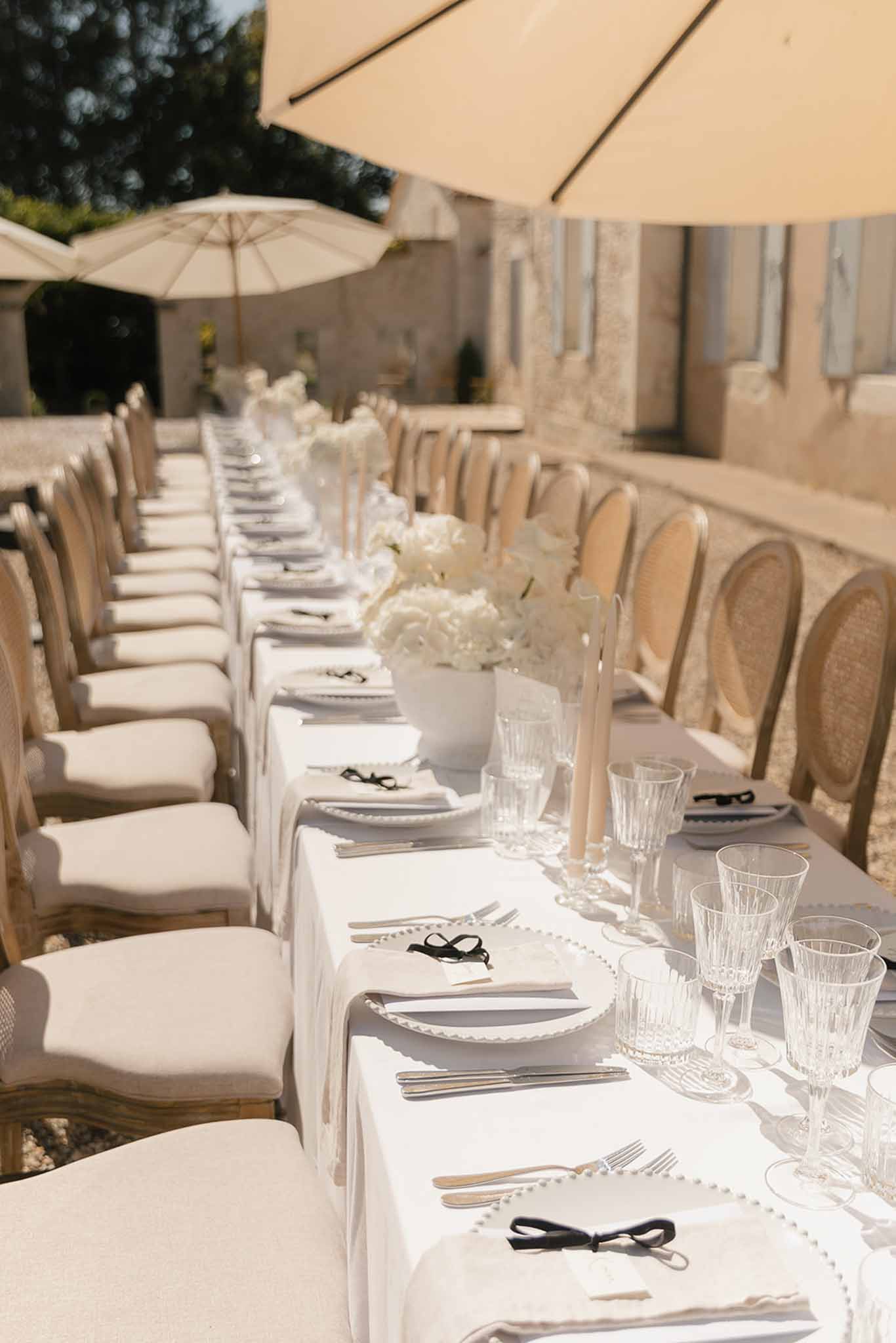 Long reception table with white linens, hydrangea centerpieces, tapered candles, and cane-back chairs