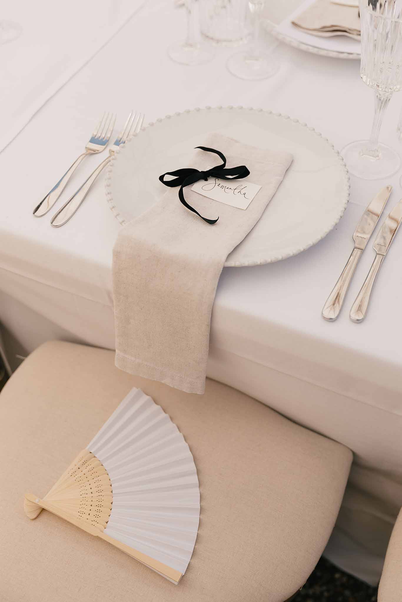 Wedding place setting with pearl-edged charger plate, calligraphy name card, black velvet ribbon, and paper fan favor