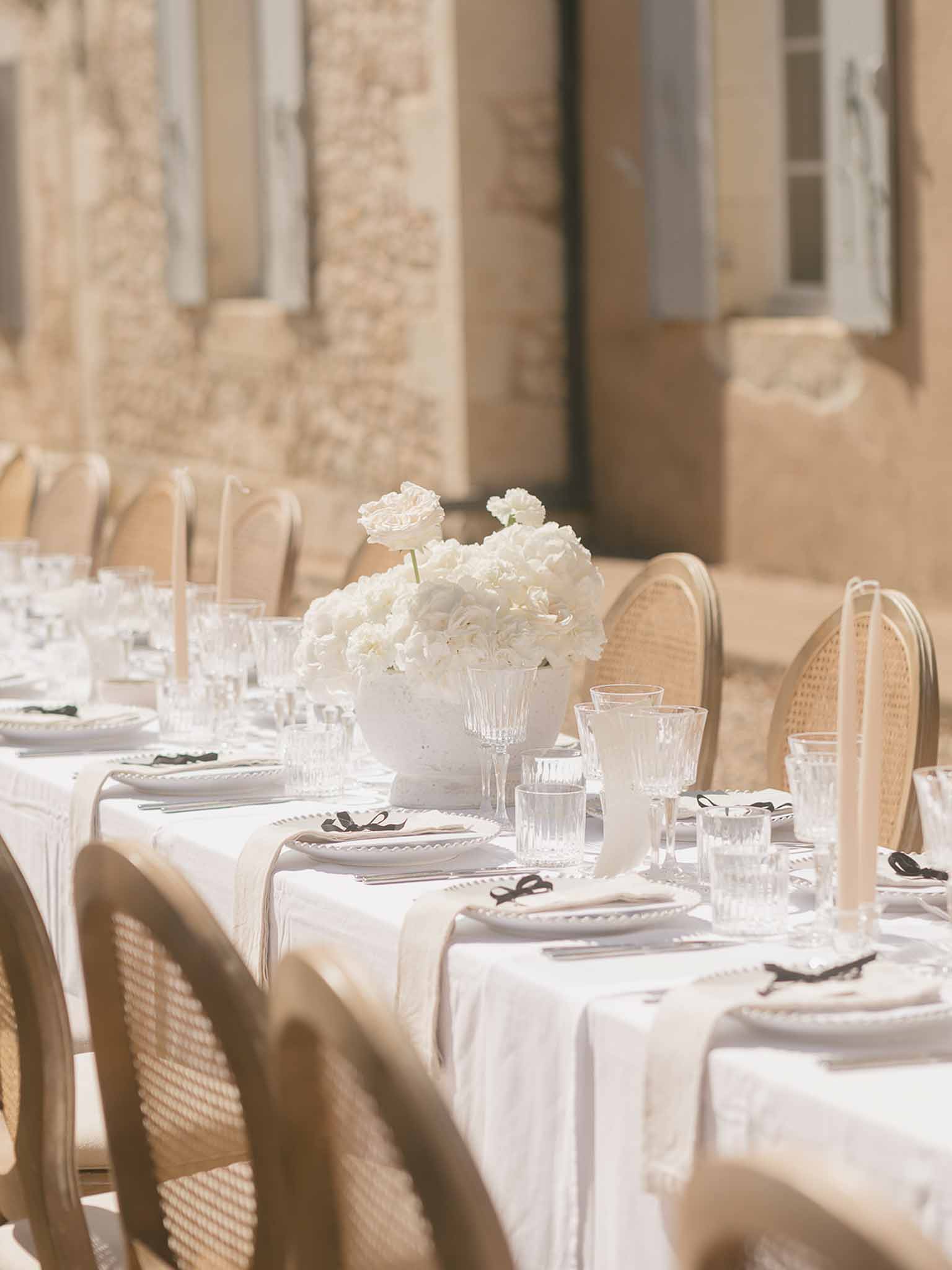White hydrangea urn centerpiece with scallop plates, black ribbon napkins, and cane-back chairs at chateau